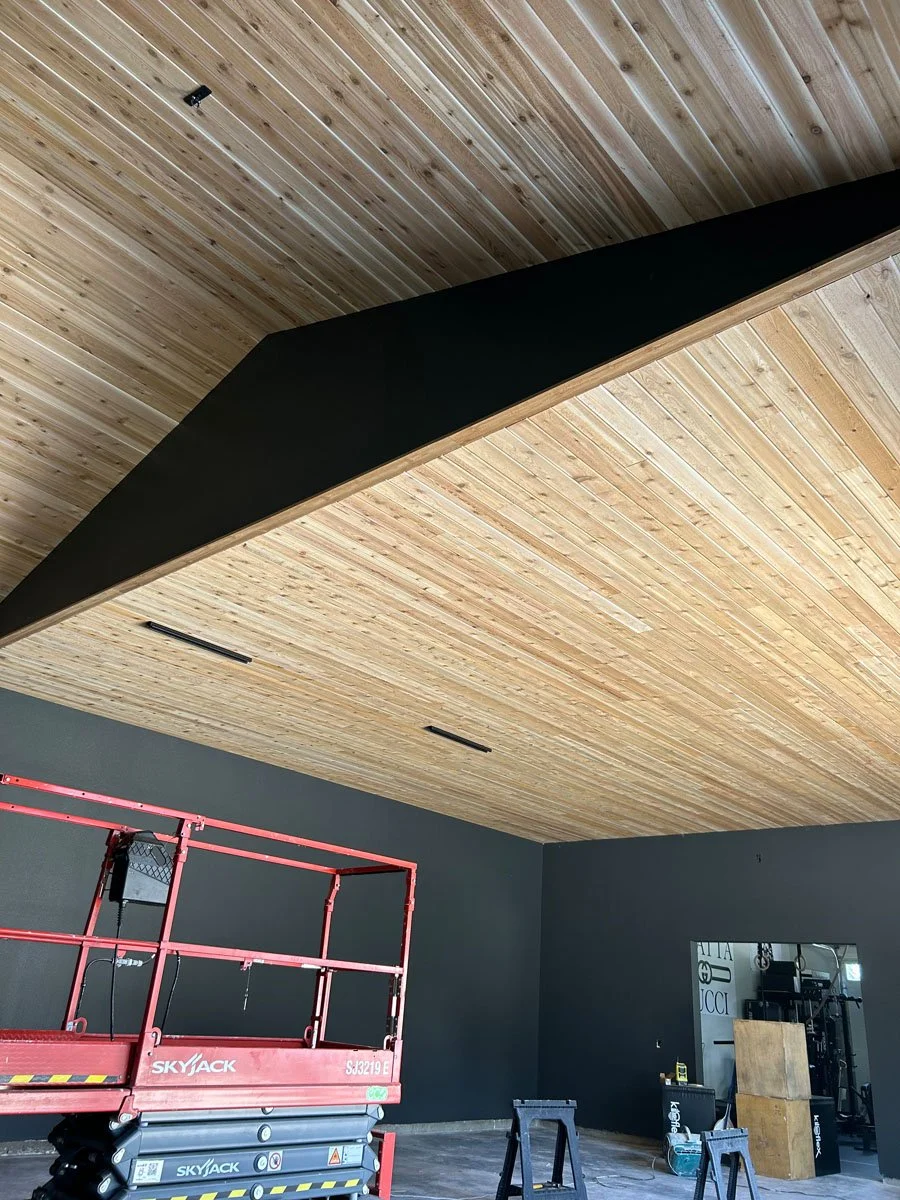 Interior room under construction with a wooden ceiling and black walls, containing construction equipment including a red scissor lift and workbenches.