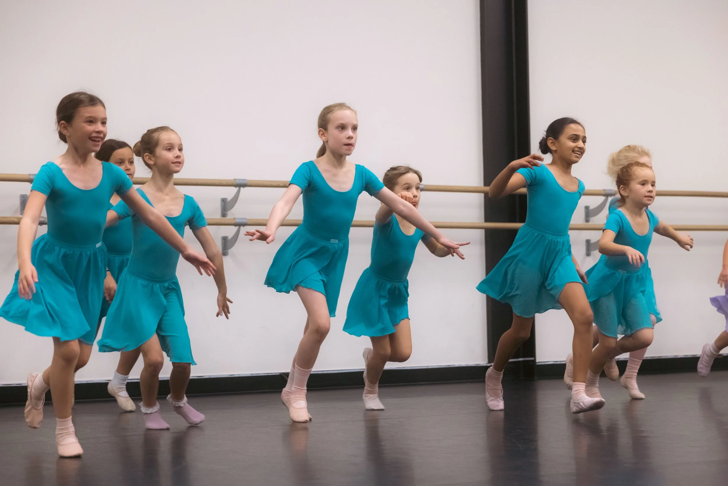Group of young girls in turquoise dance costumes practicing ballet in a dance studio