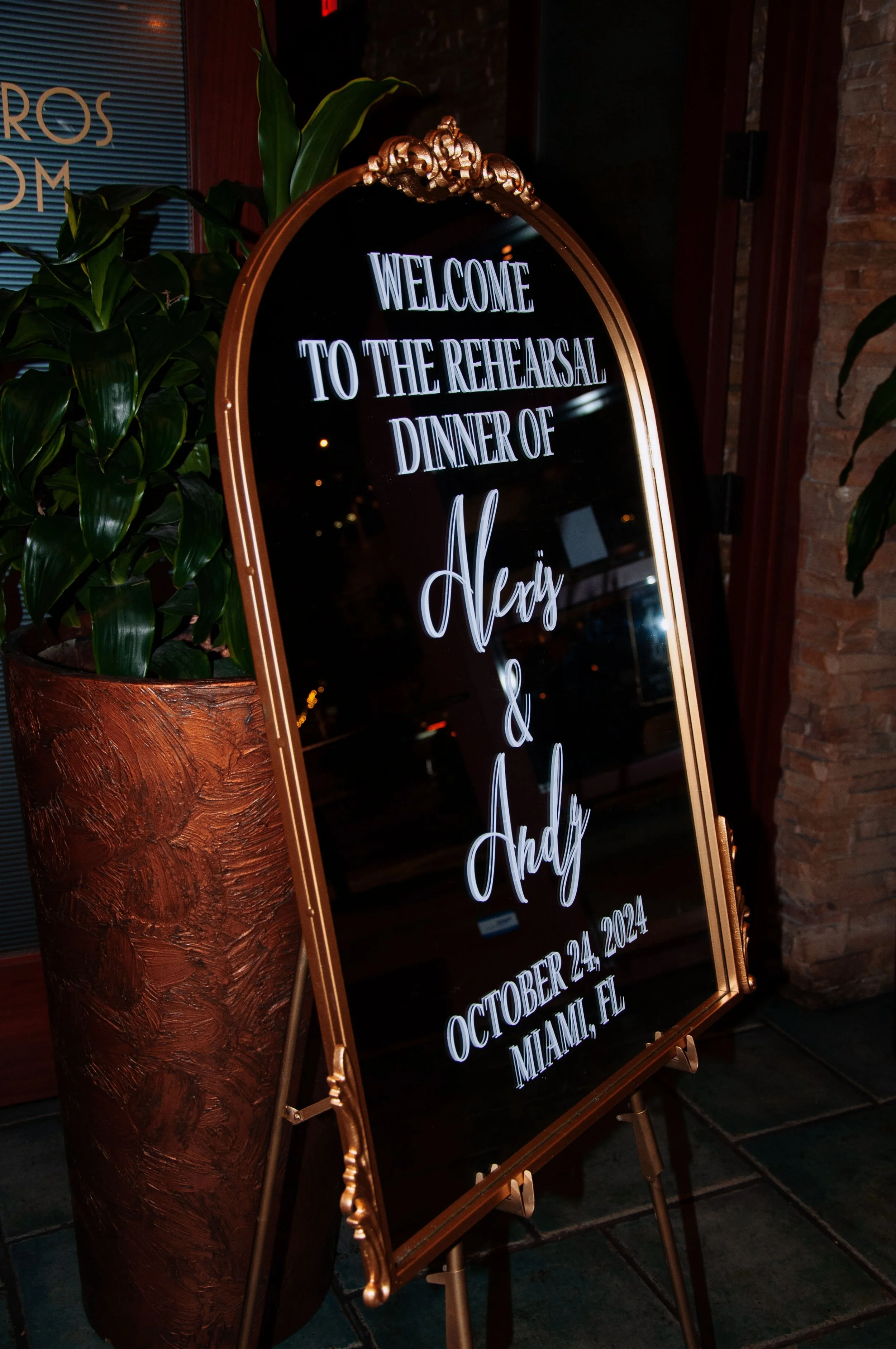 Sign welcoming guests to a rehearsal dinner for Alexis and Andy on October 24, 2024, in Miami, FL, displayed on an easel beside plants.