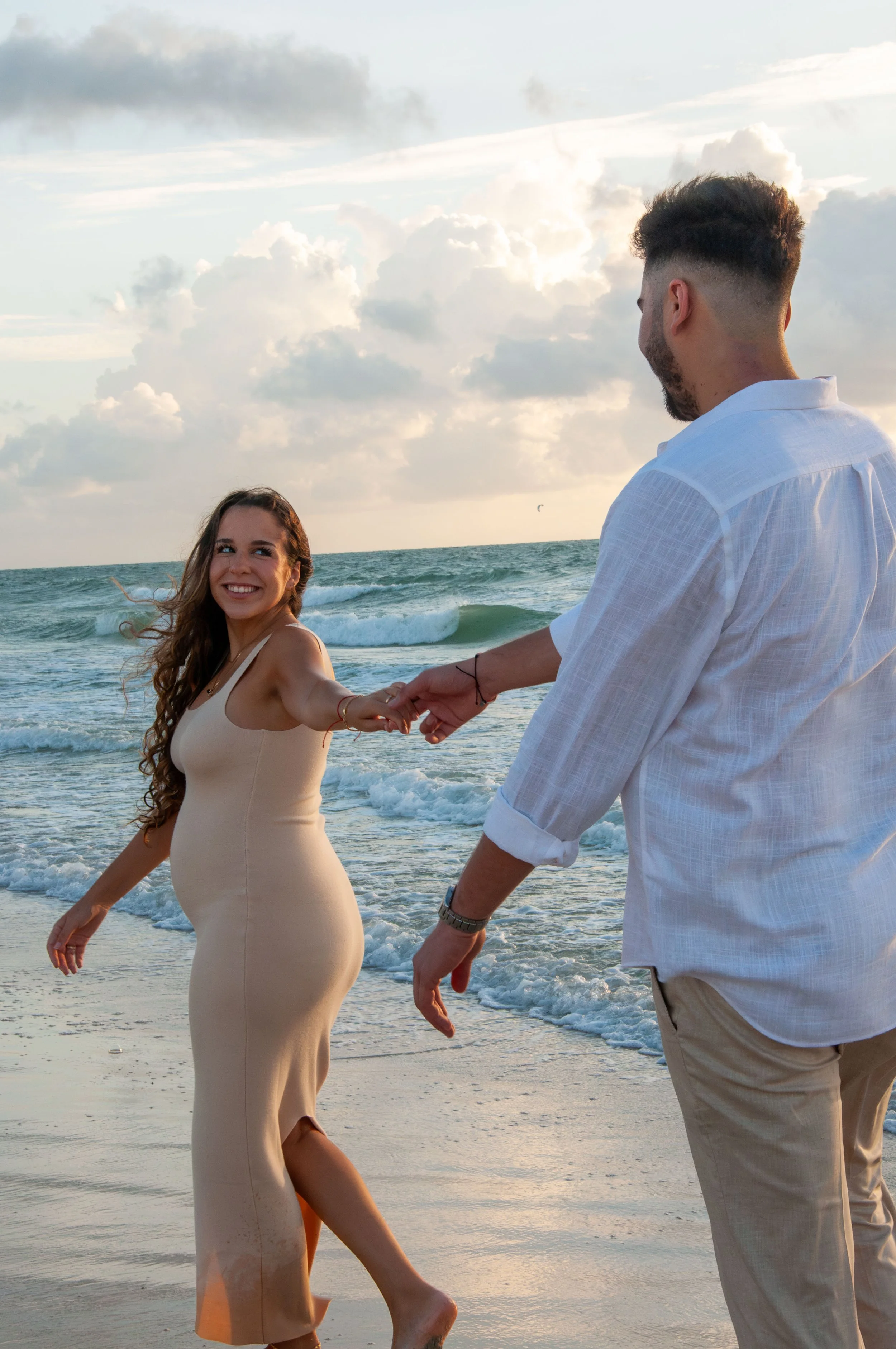 A couple holding hands walking on a beach at sunset.