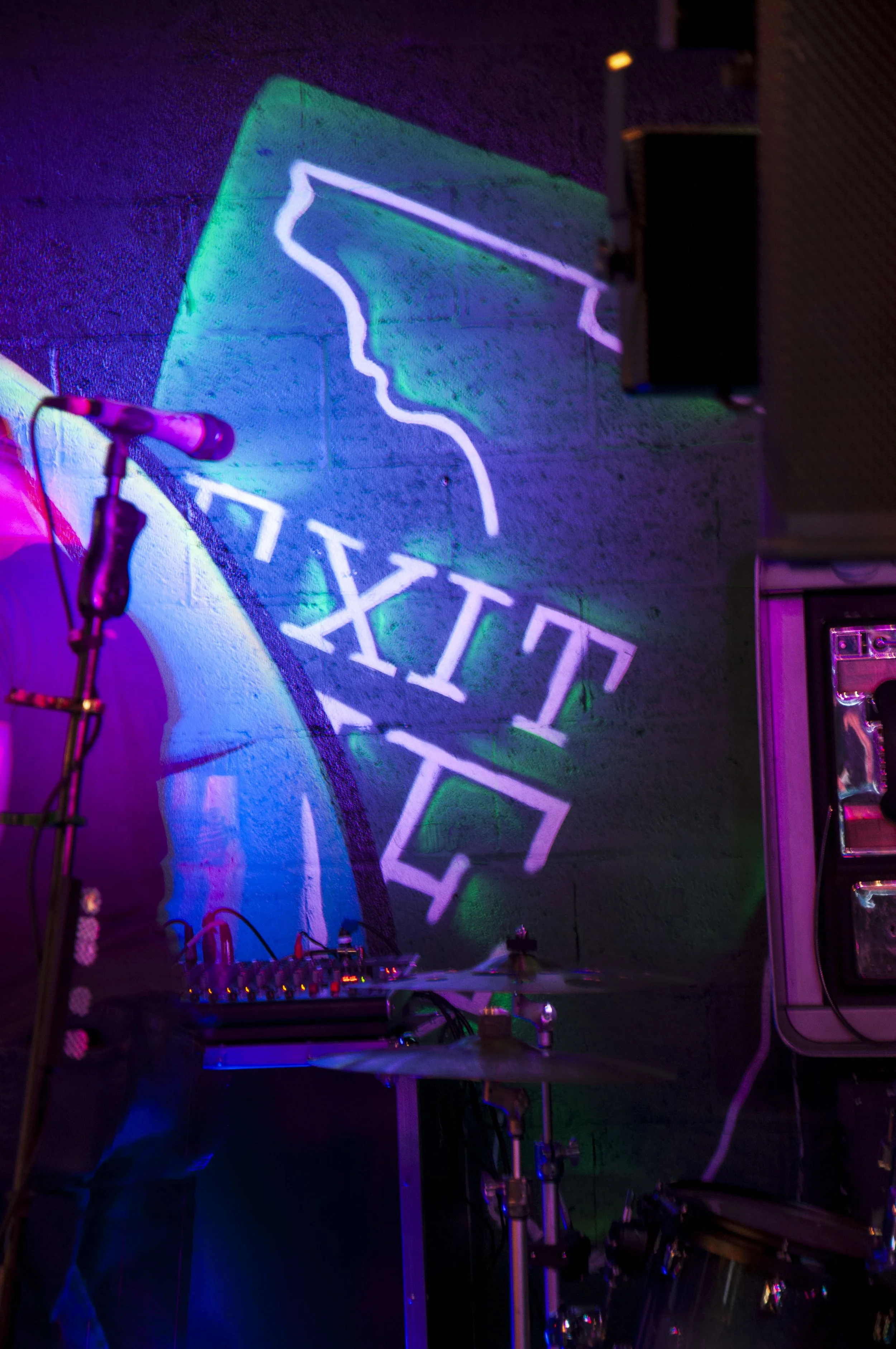 Dimly lit stage with microphone, drum set, and "EXIT" sign