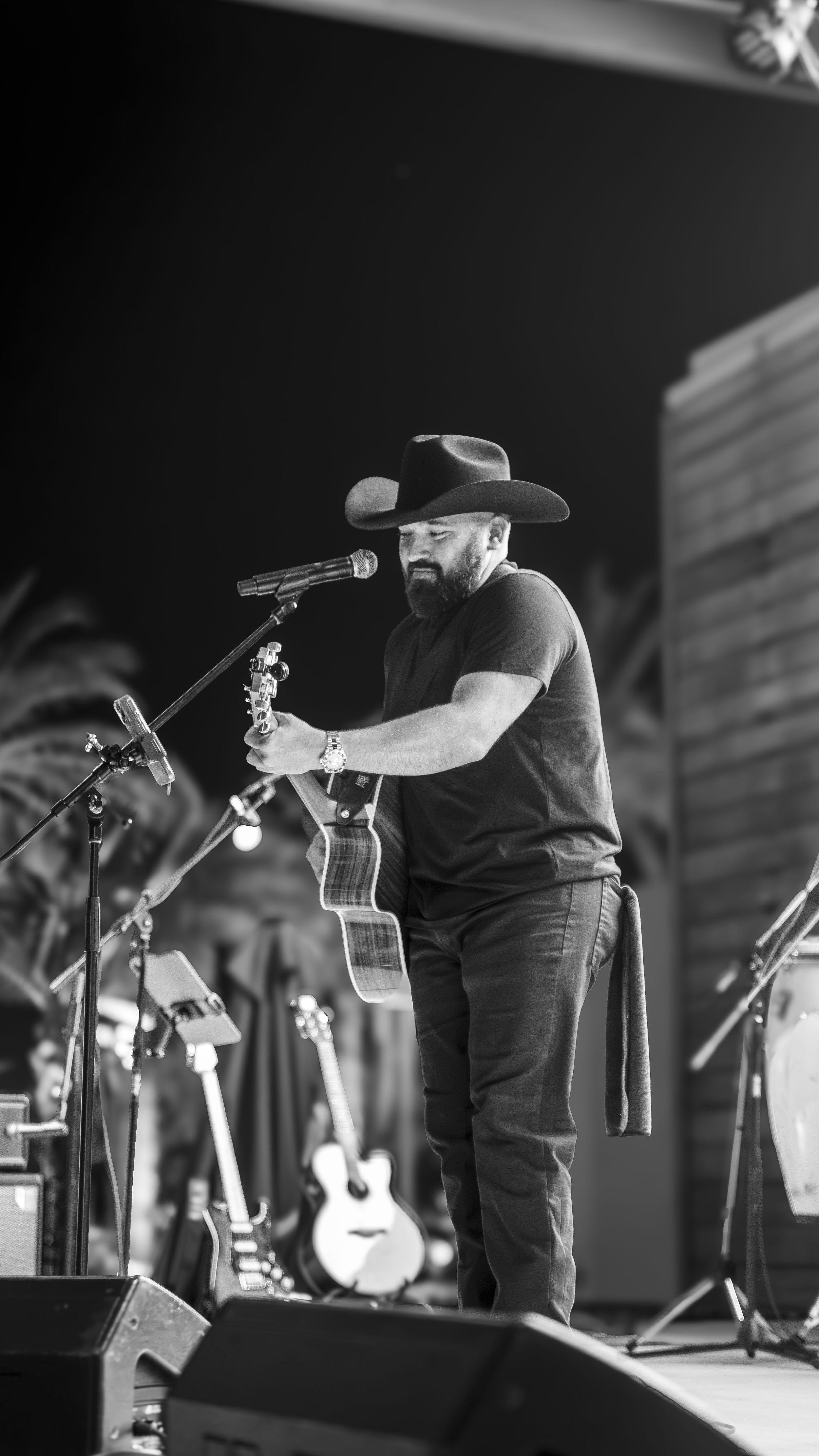 Black and white photo of a man in a cowboy hat playing guitar and singing into a microphone on stage.