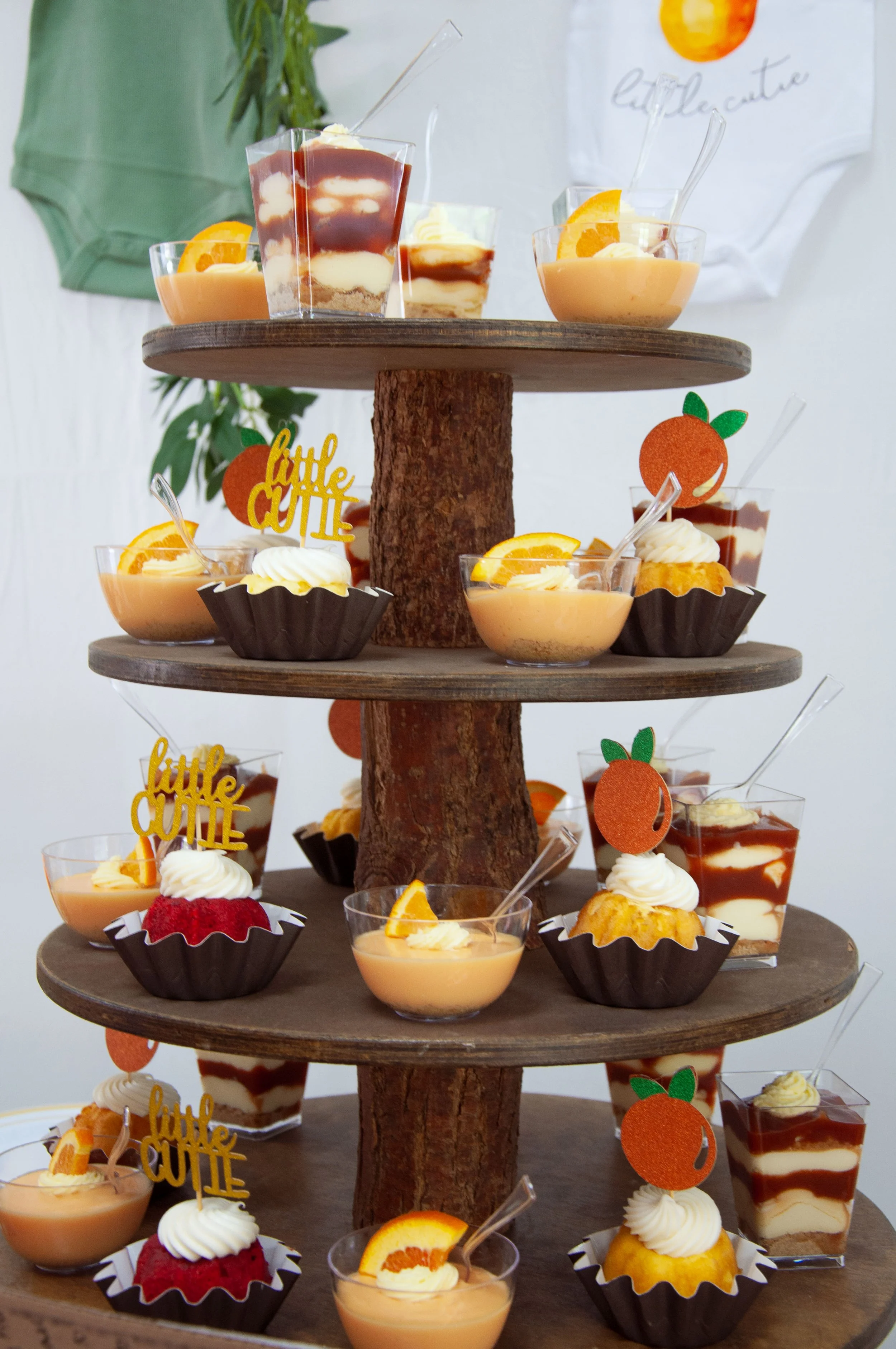 Dessert display with layered puddings, cupcakes with cream and orange garnishes, and 'little cutie' signs.