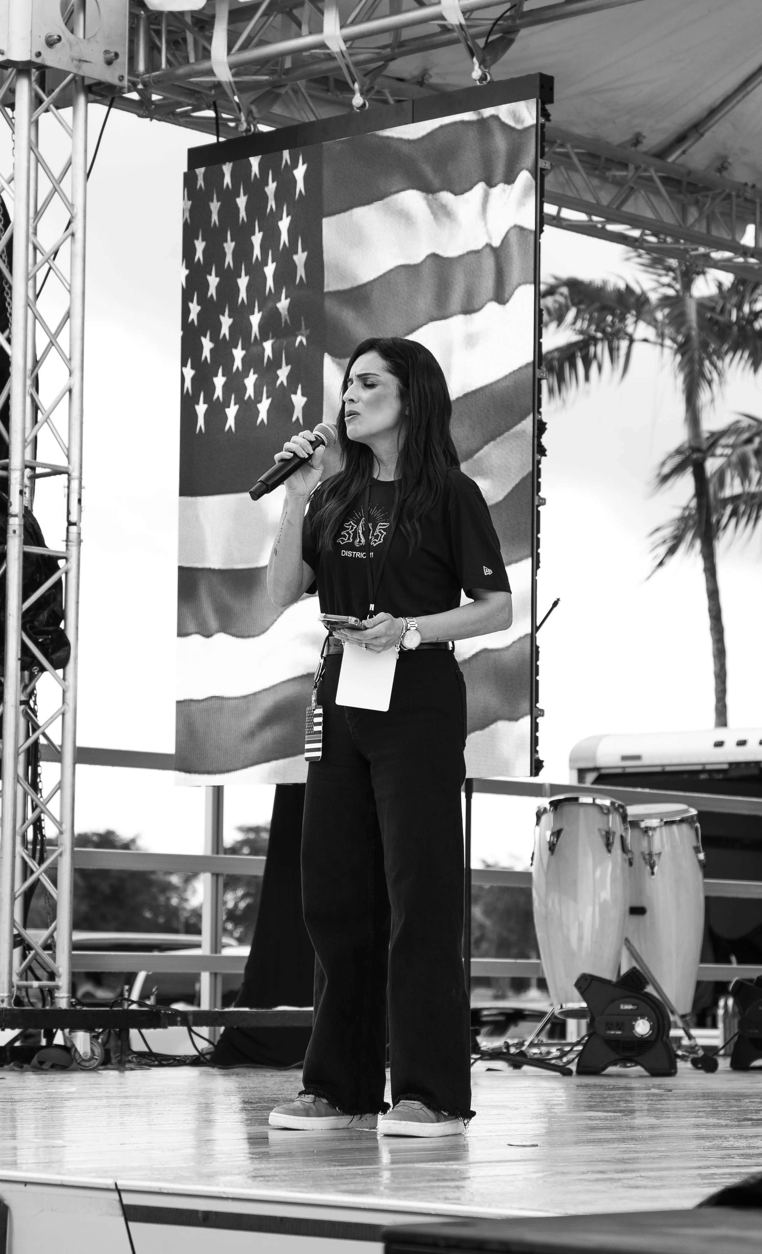 Musician wearing a black hat and shirt playing an acoustic guitar and singing into a microphone on stage.