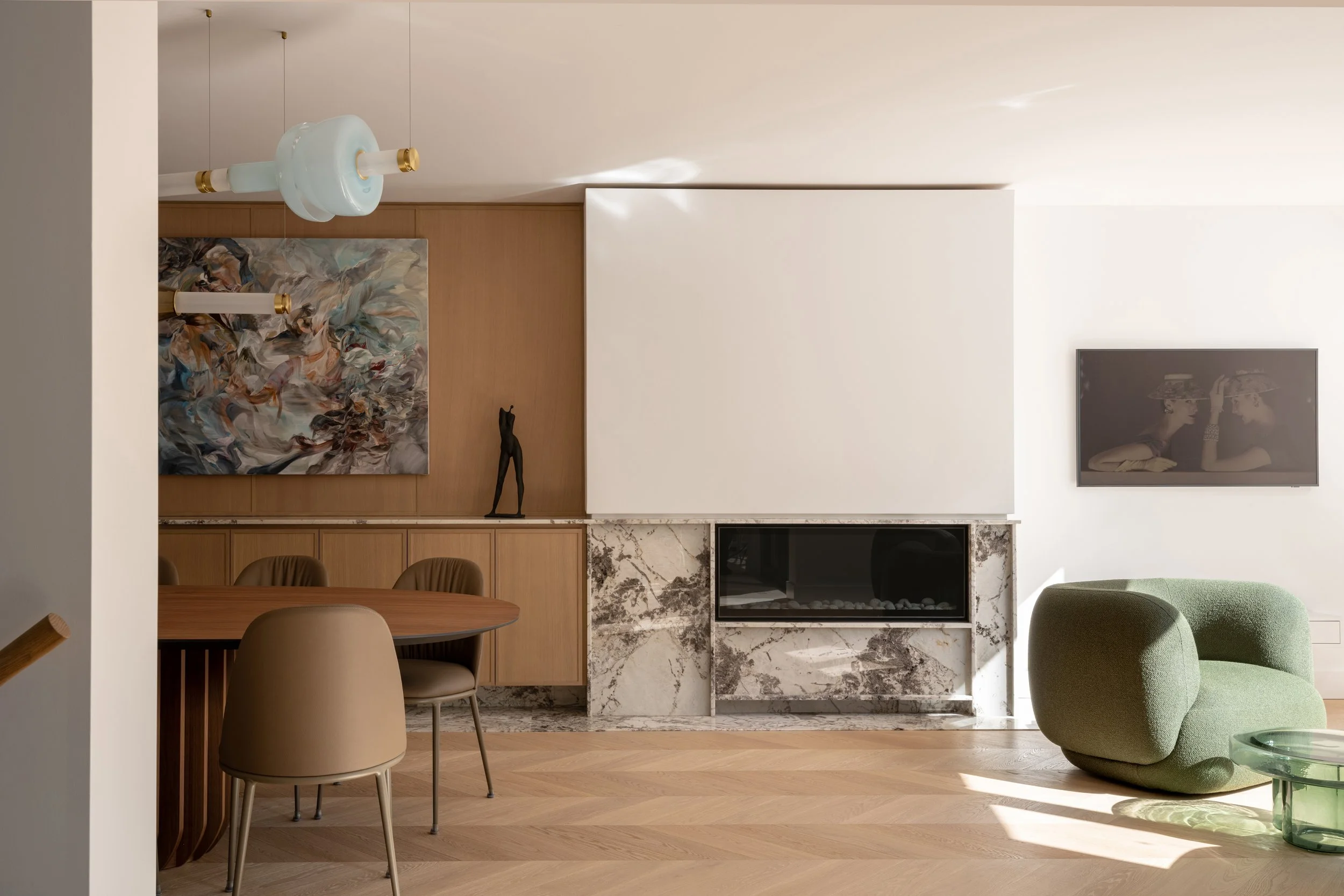 Modern living room with abstract artwork, fireplace with marble surround, and green plush chair.