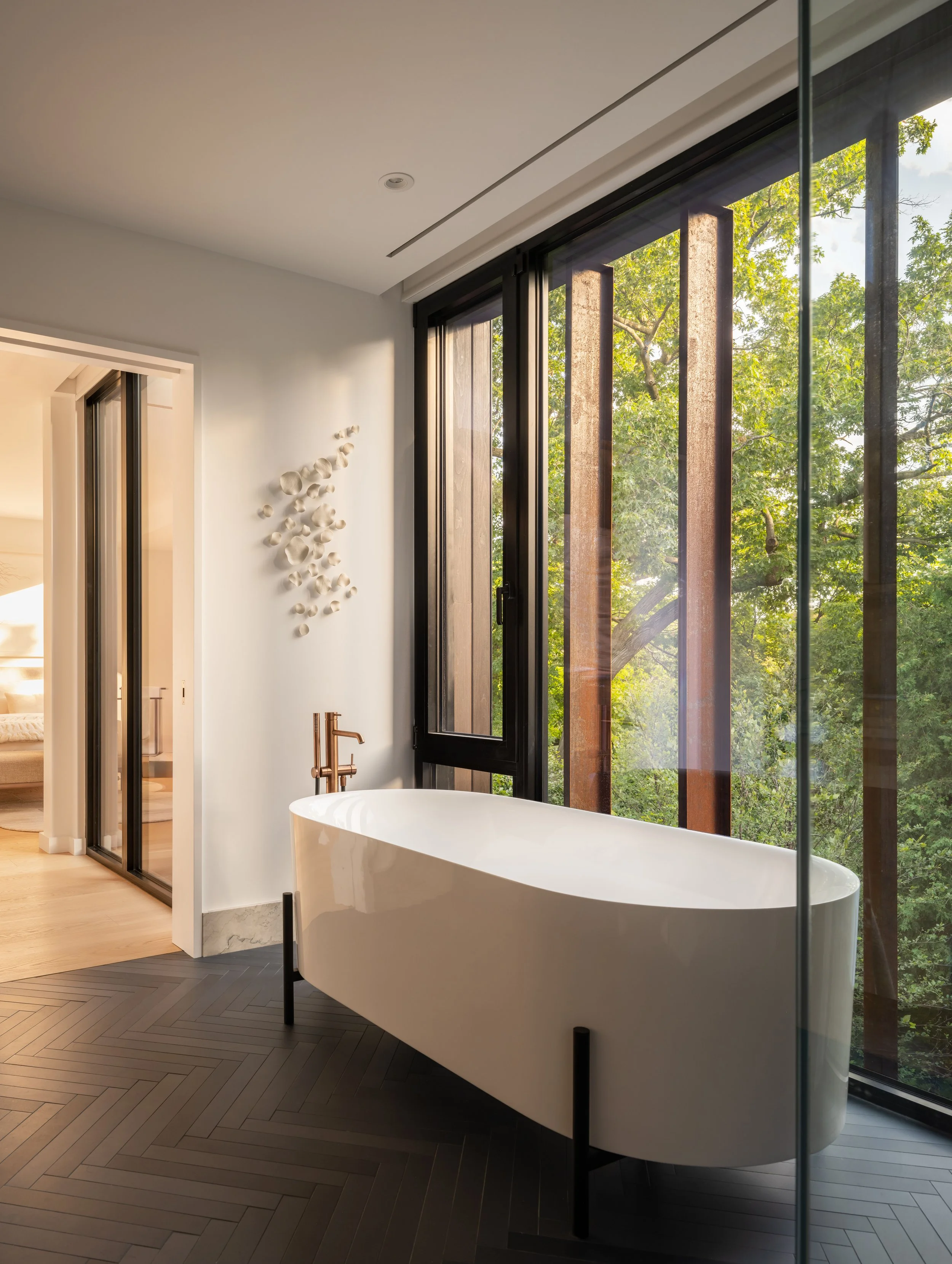 Modern bathroom featuring a freestanding bathtub, large window with views of trees, blue herringbone-patterned tile floor and corten metal exterior fins.