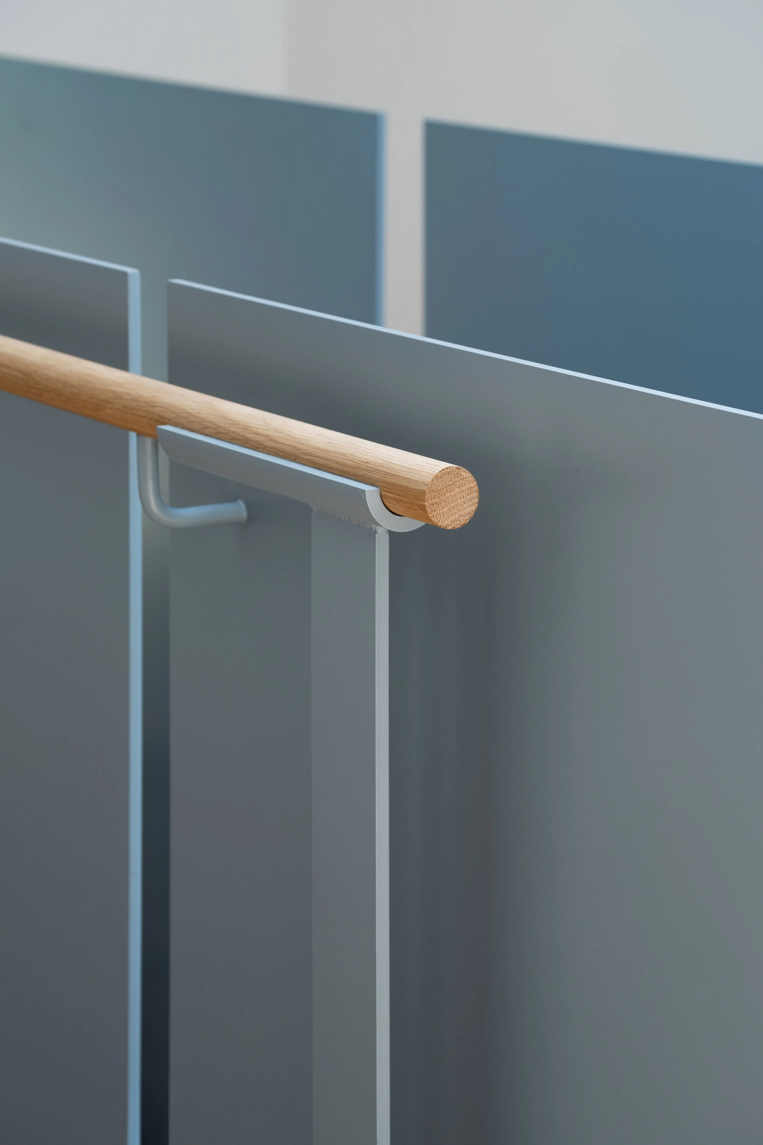 Close-up of a wooden handrail attached to a blue steel guard with a metal bracket, part of a staircase and hallway railing.