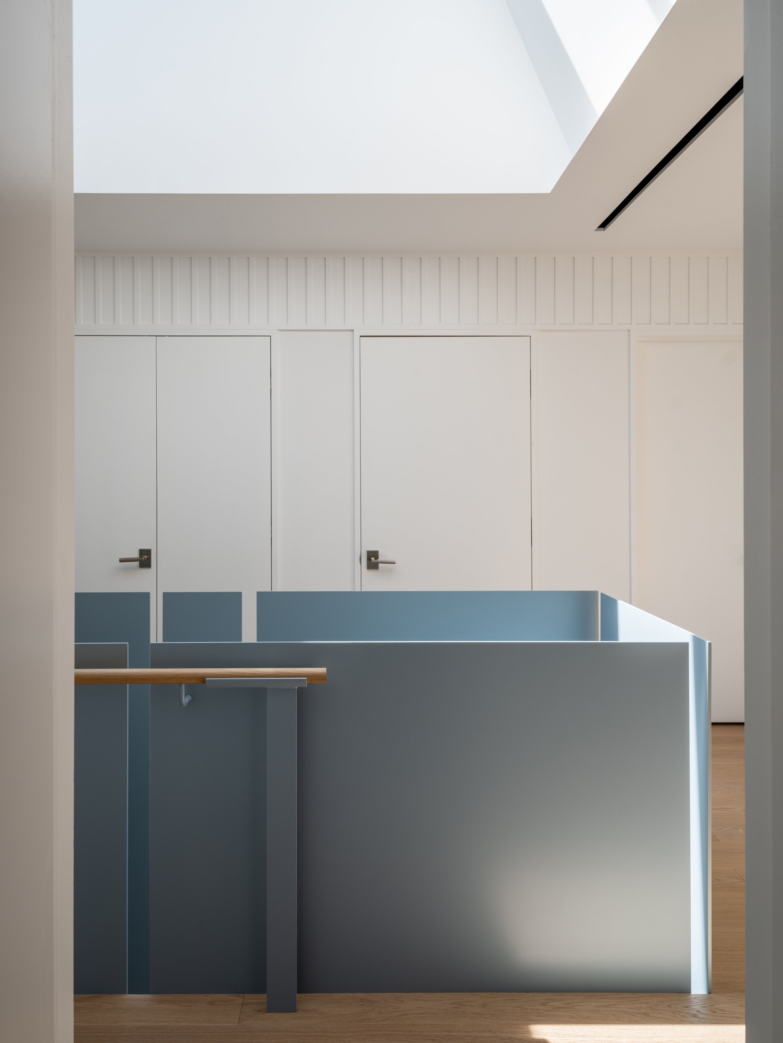 Interior view of a modern, minimalist home with white walls, a skylight, and a stairway with a wooden handrail and blue steel guards.