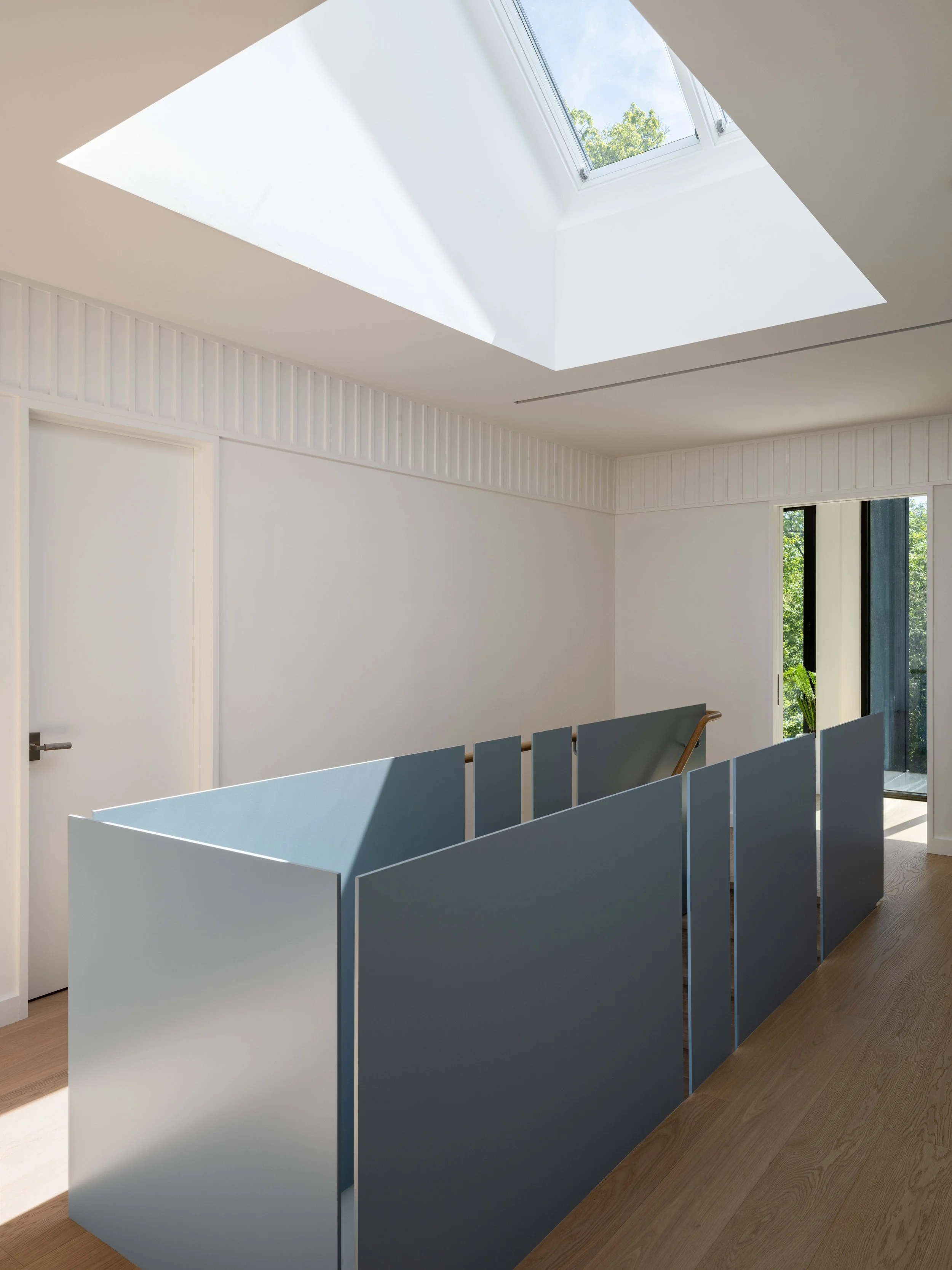 An interior room with a skylight window on the ceiling and a partial view of a pocket door, wood floor, with greenery outside.