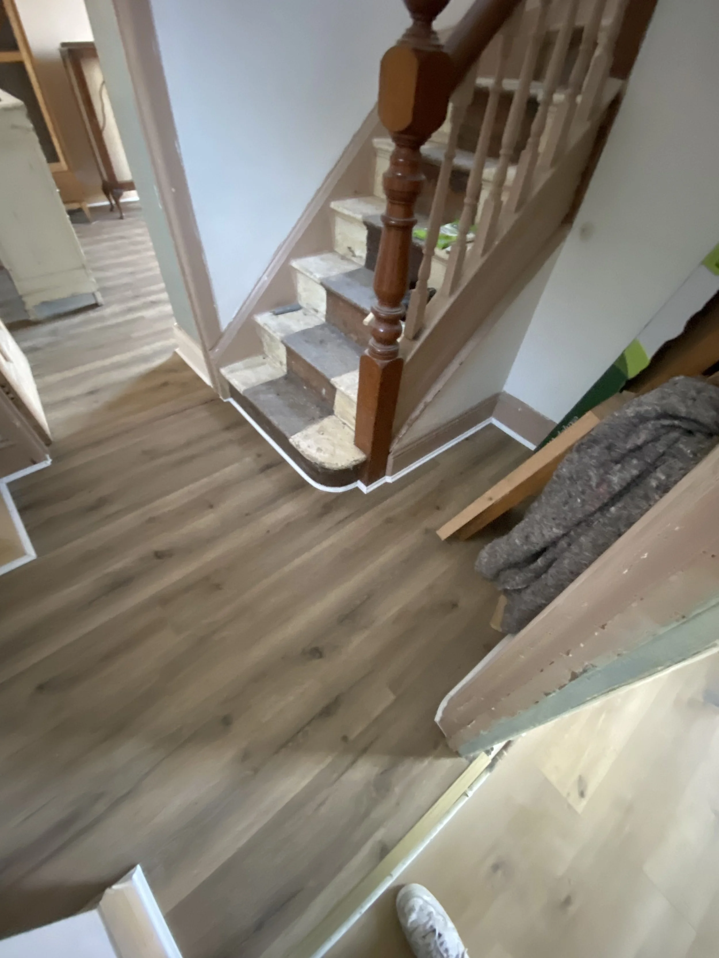 View of a staircase under construction with exposed stairs and partial wood railing, adjacent to a freshly installed wood floor in a house interior.
