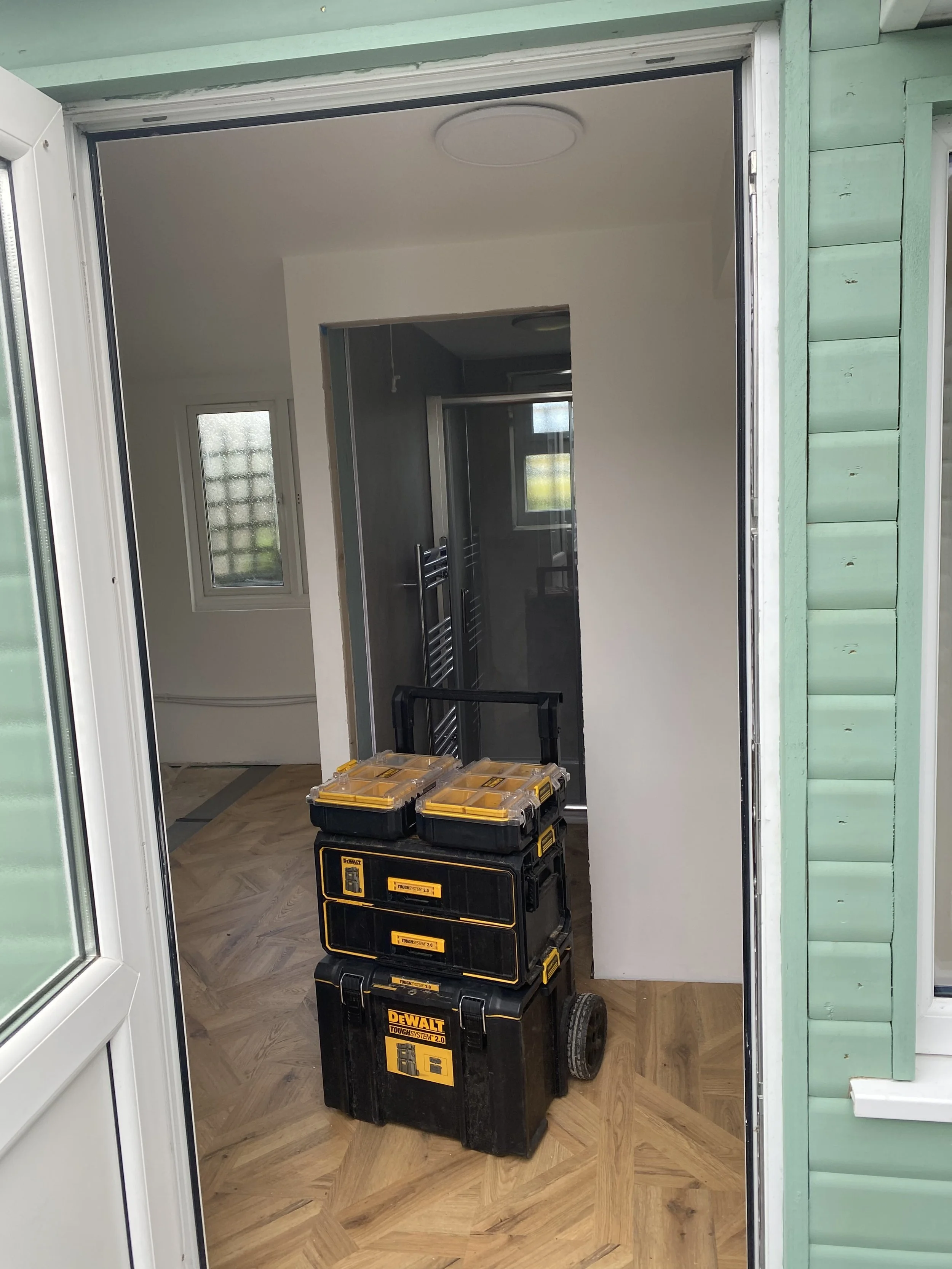 View through a doorway showing a toolbox on wheels with yellow and black colors inside a room under renovation, with a towel radiator and window in the background.