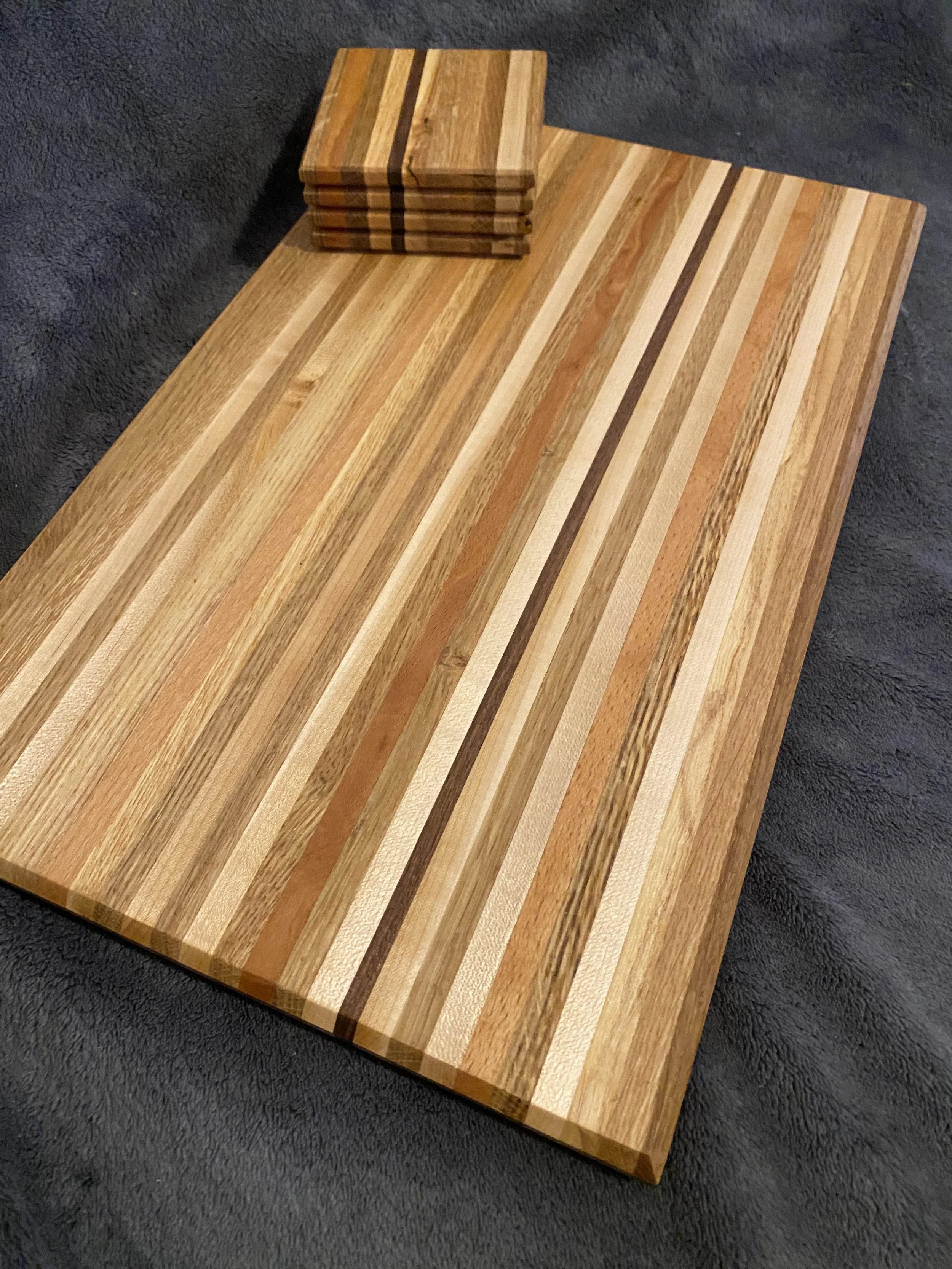 Several wooden cutting boards with striped patterns, stacked on a larger cutting board, placed on a dark textured surface.