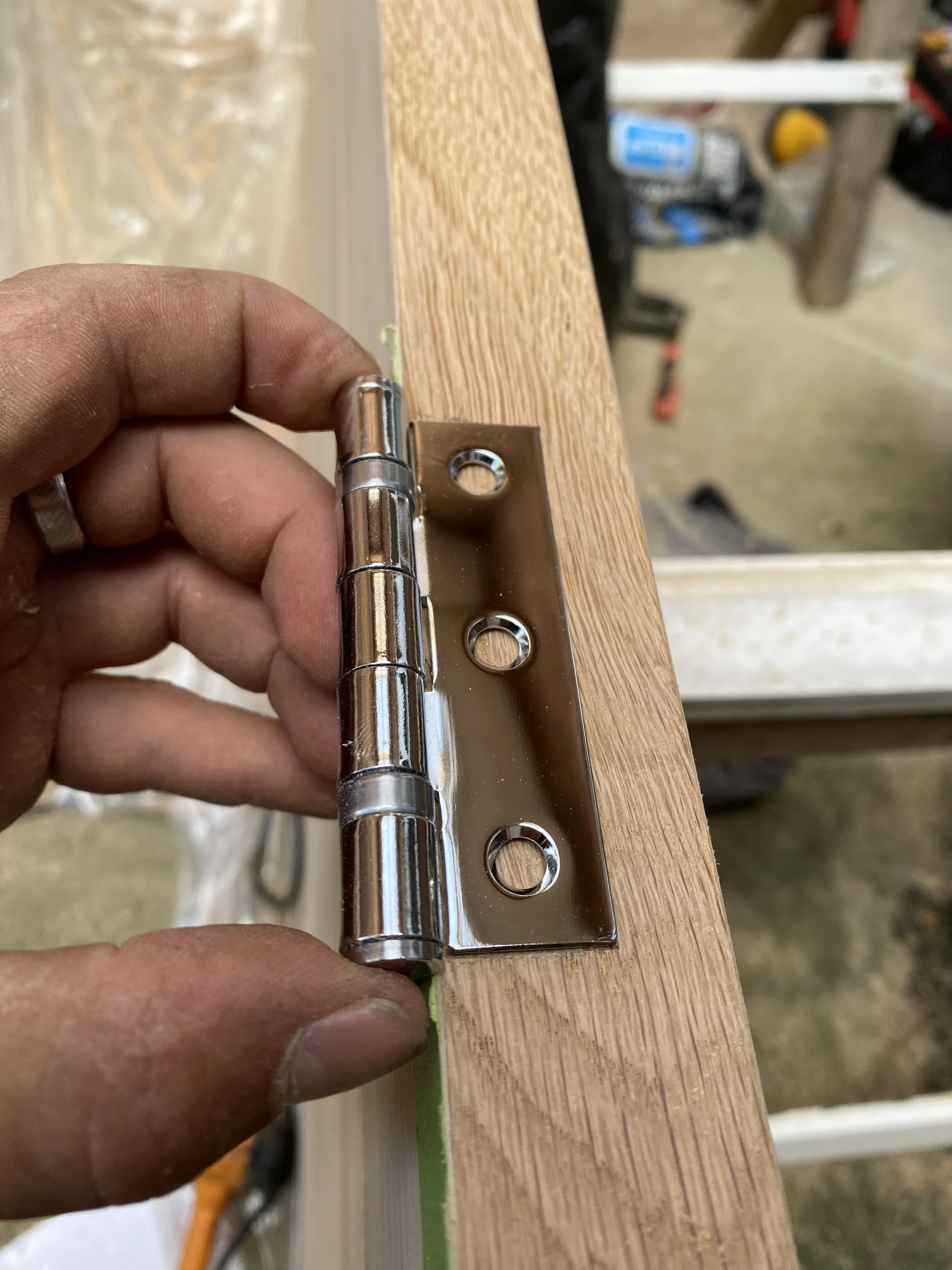 A close-up of a person installing a metal hinge onto a wooden surface in a workshop.