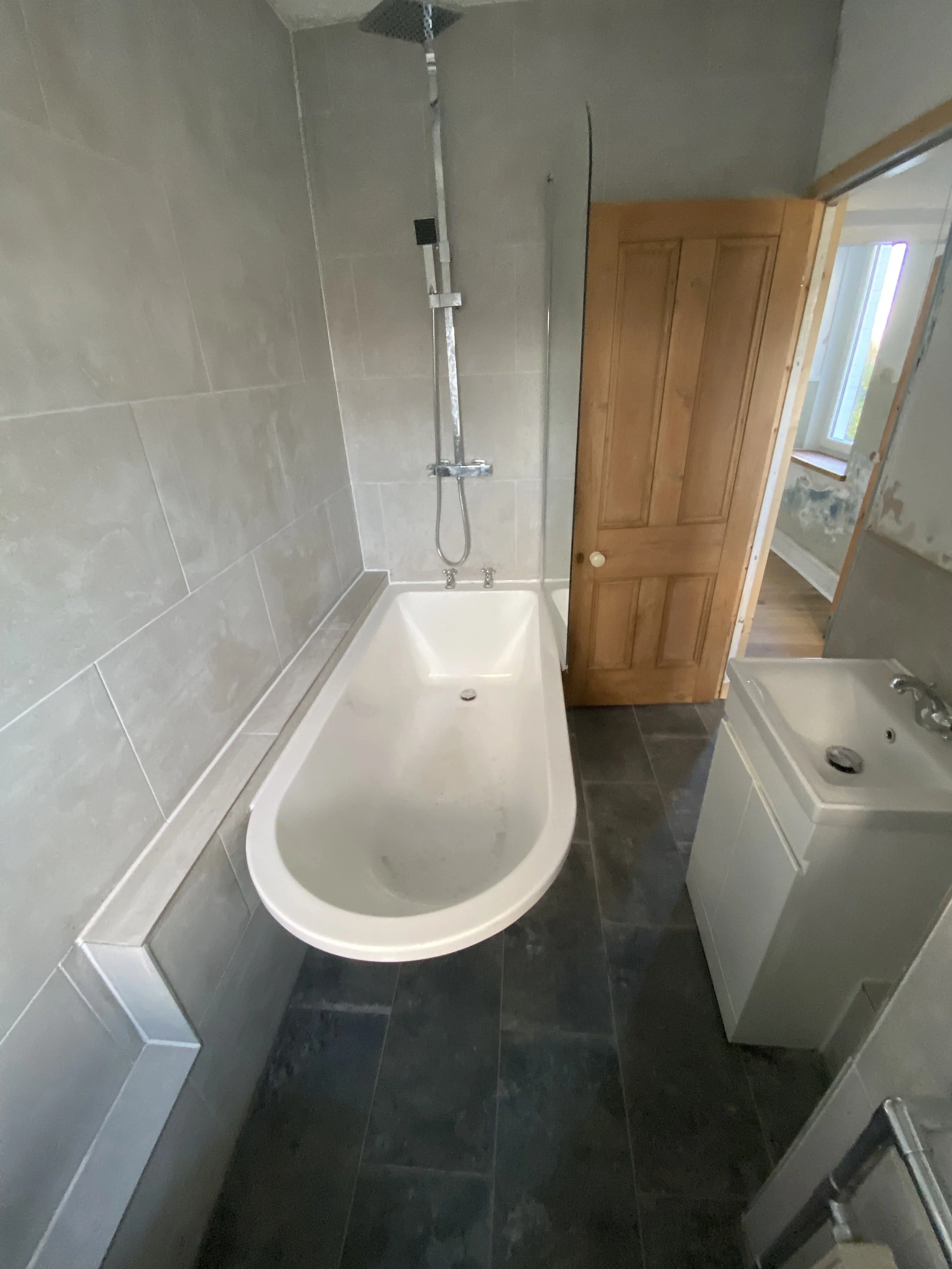 Empty bathroom with a bathtub, shower head, sink, and wooden door, in a room under renovation.