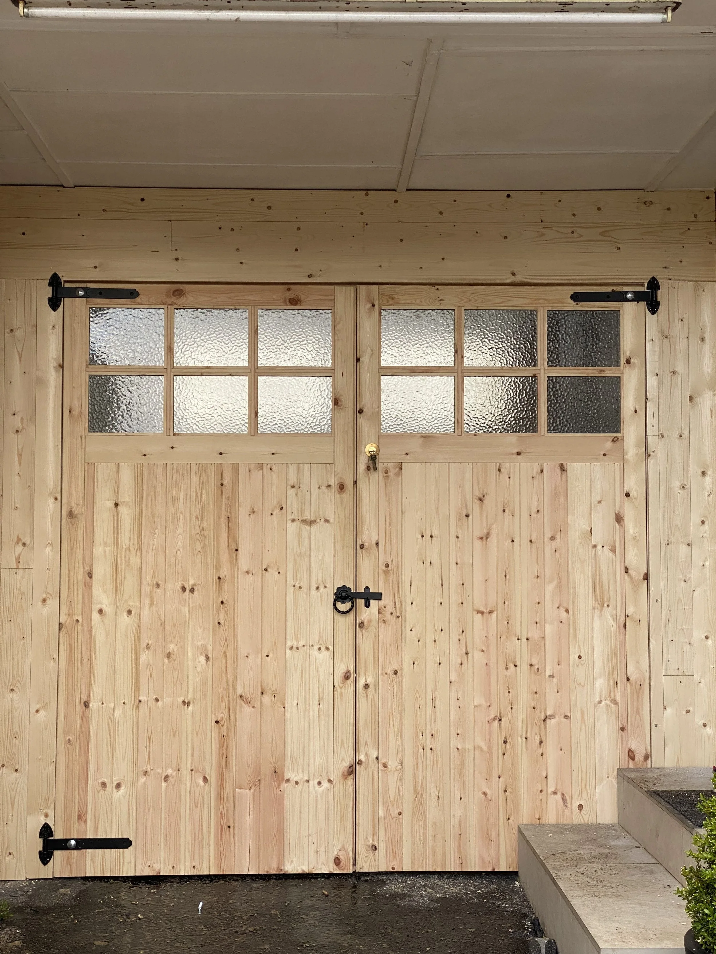 Wooden double doors with glass panels on top, metal hardware, and a lock in the center. The doors are part of a wooden structure with steps leading up to the right.