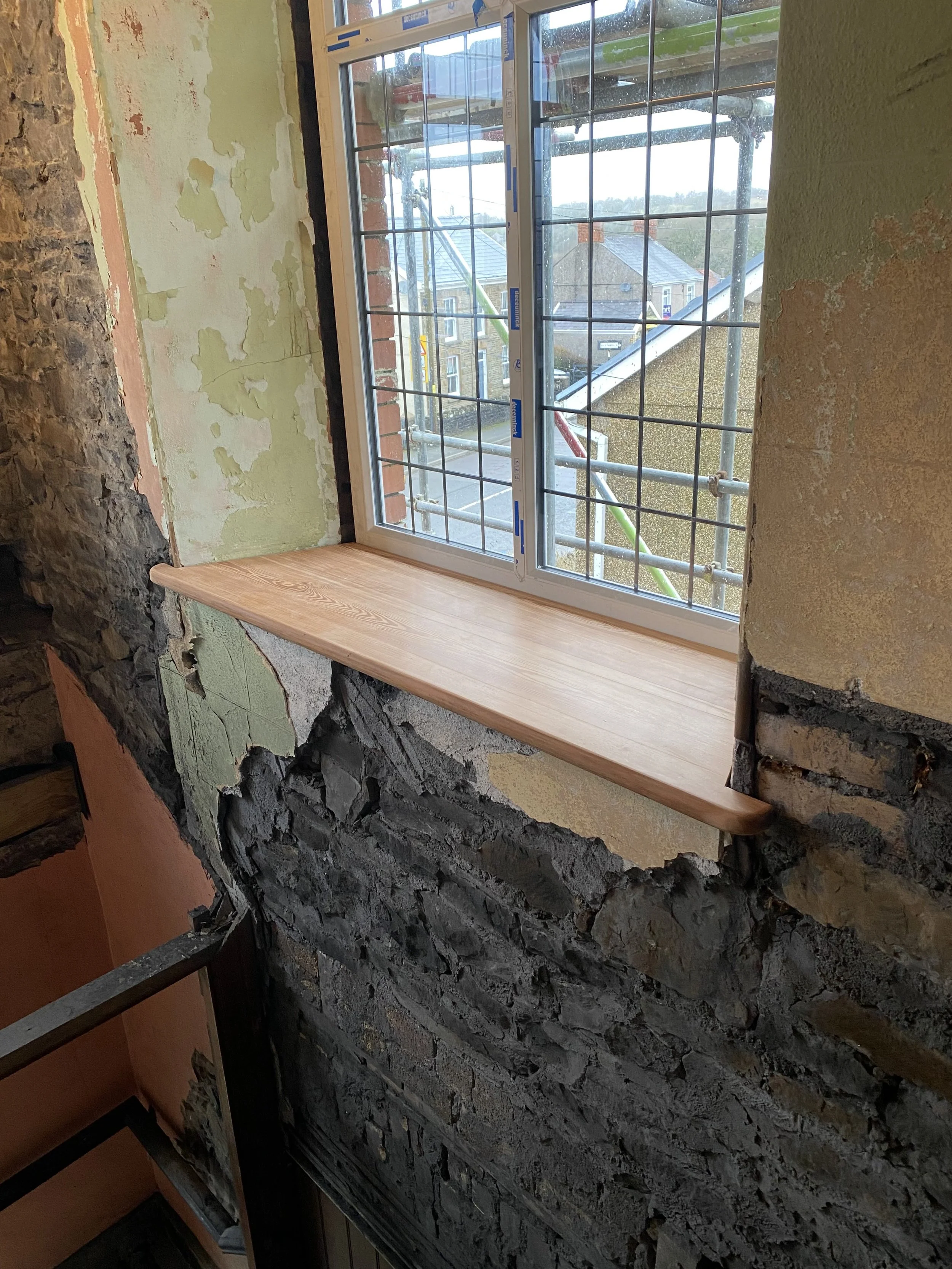 Indoor construction site with a new wooden window sill installed in a wall with exposed brick and plaster.