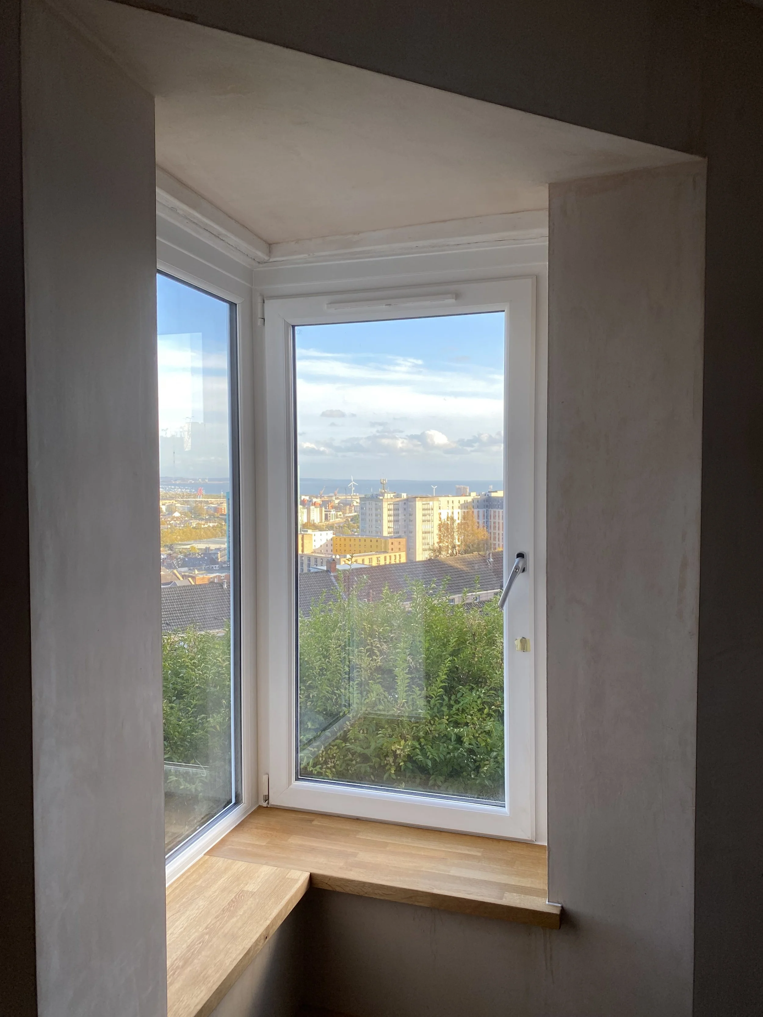 View through a window overlooking a cityscape with buildings, trees, and a partly cloudy sky.