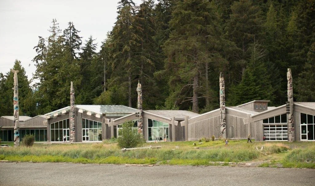 Modern building with large windows and totem poles in forest setting