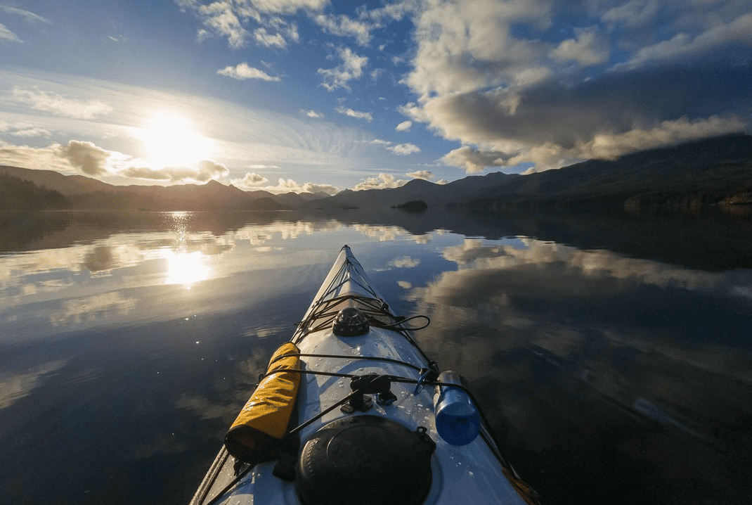 Kayak on a calm lake at sunset with mountain and sky reflections in the water.