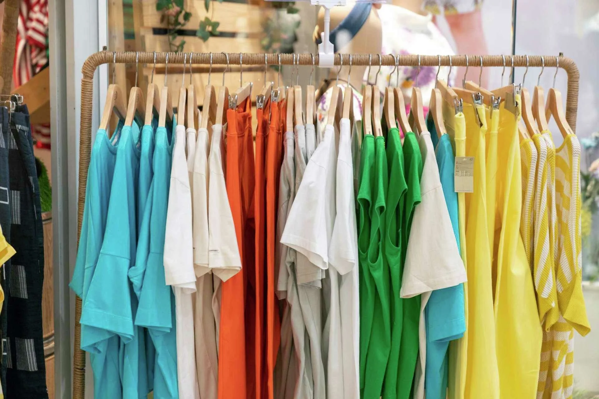 Colorful shirts and dresses hanging on a rack in a clothing store.