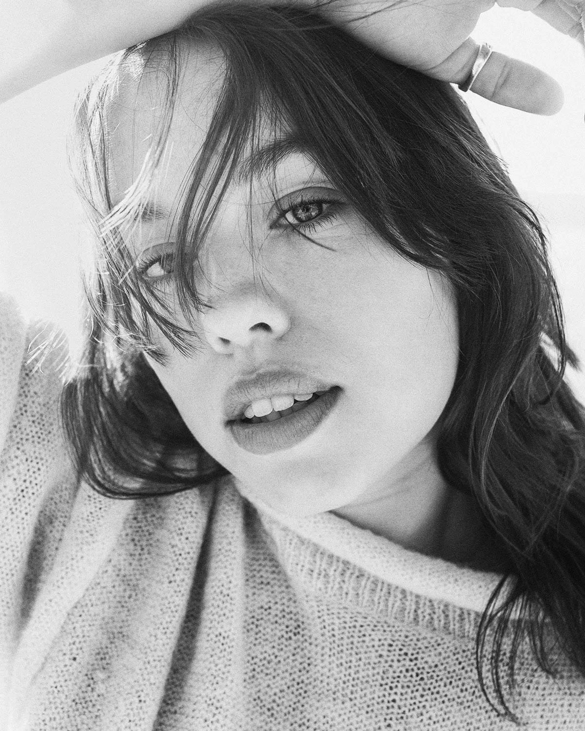 Black and white close-up of a young woman with wavy hair, partially covering one eye, looking at the camera with her lips slightly parted.