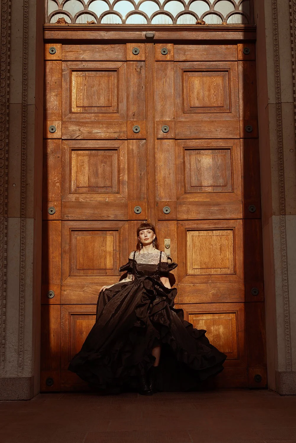 A woman in a black dress standing in front of a large wooden door.