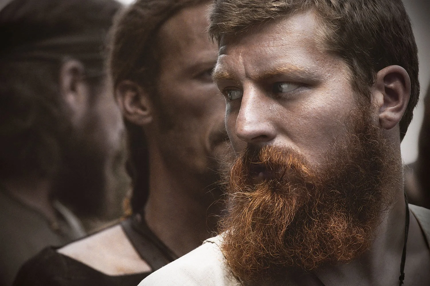Close-up of three people with serious expressions, two women and one man with a reddish beard, in a candid moment.