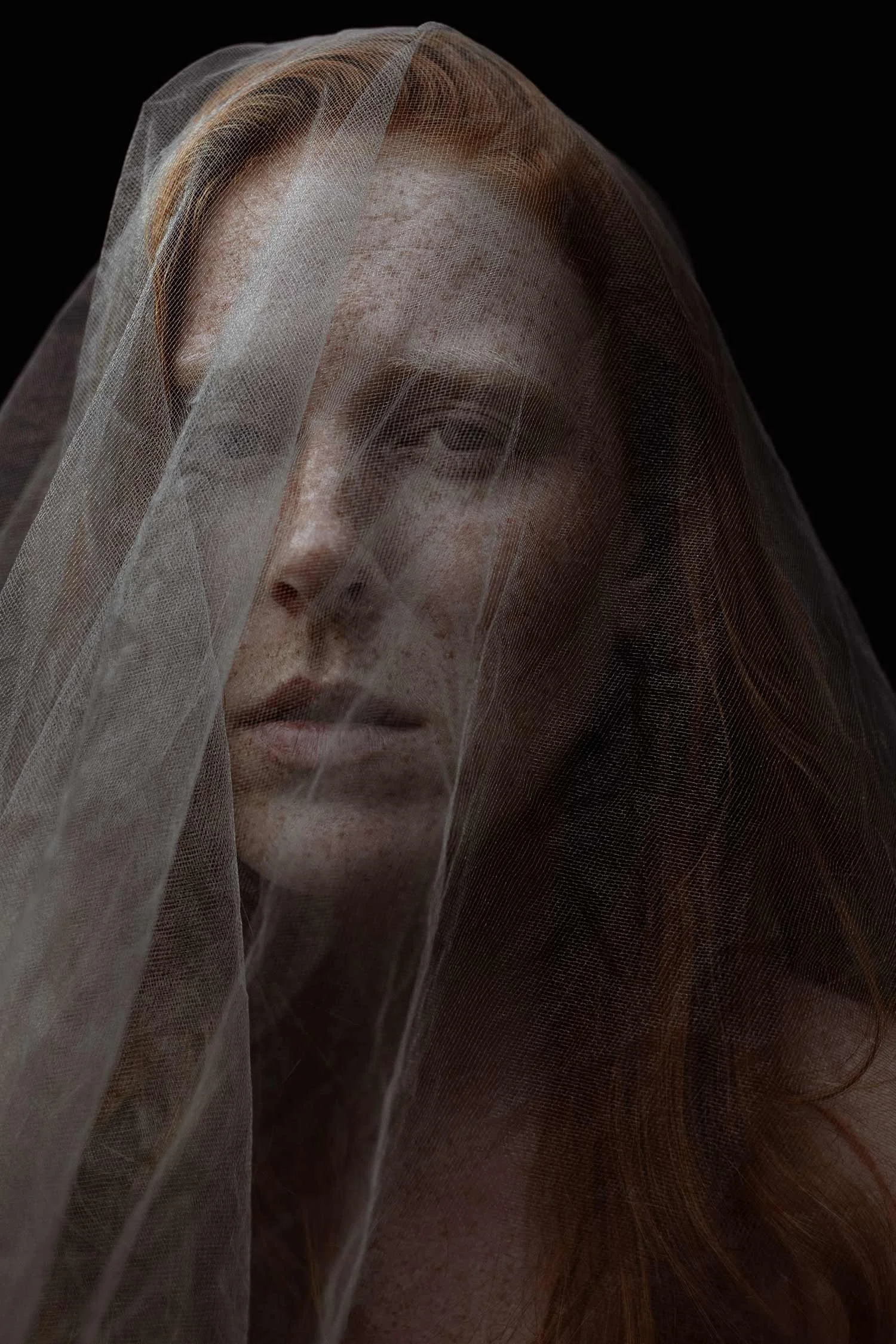 Close-up of a woman with red hair behind sheer fabric, with a dark background.
