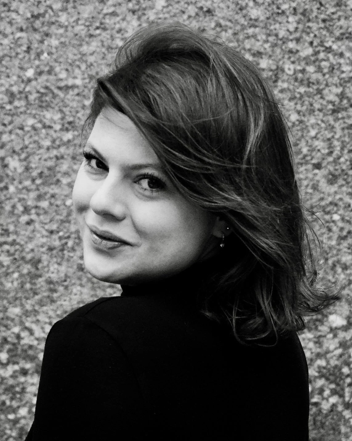 A black and white photo of a woman with shoulder-length hair smiling, looking over her shoulder.