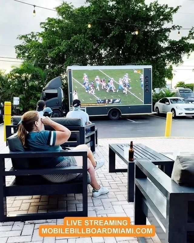Fans watching a live football game streamed on a digital billboard truck screen
