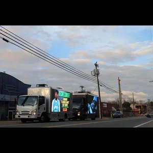 White campaign vehicle with digital LED screens parked on a city street under a partly cloudy sky