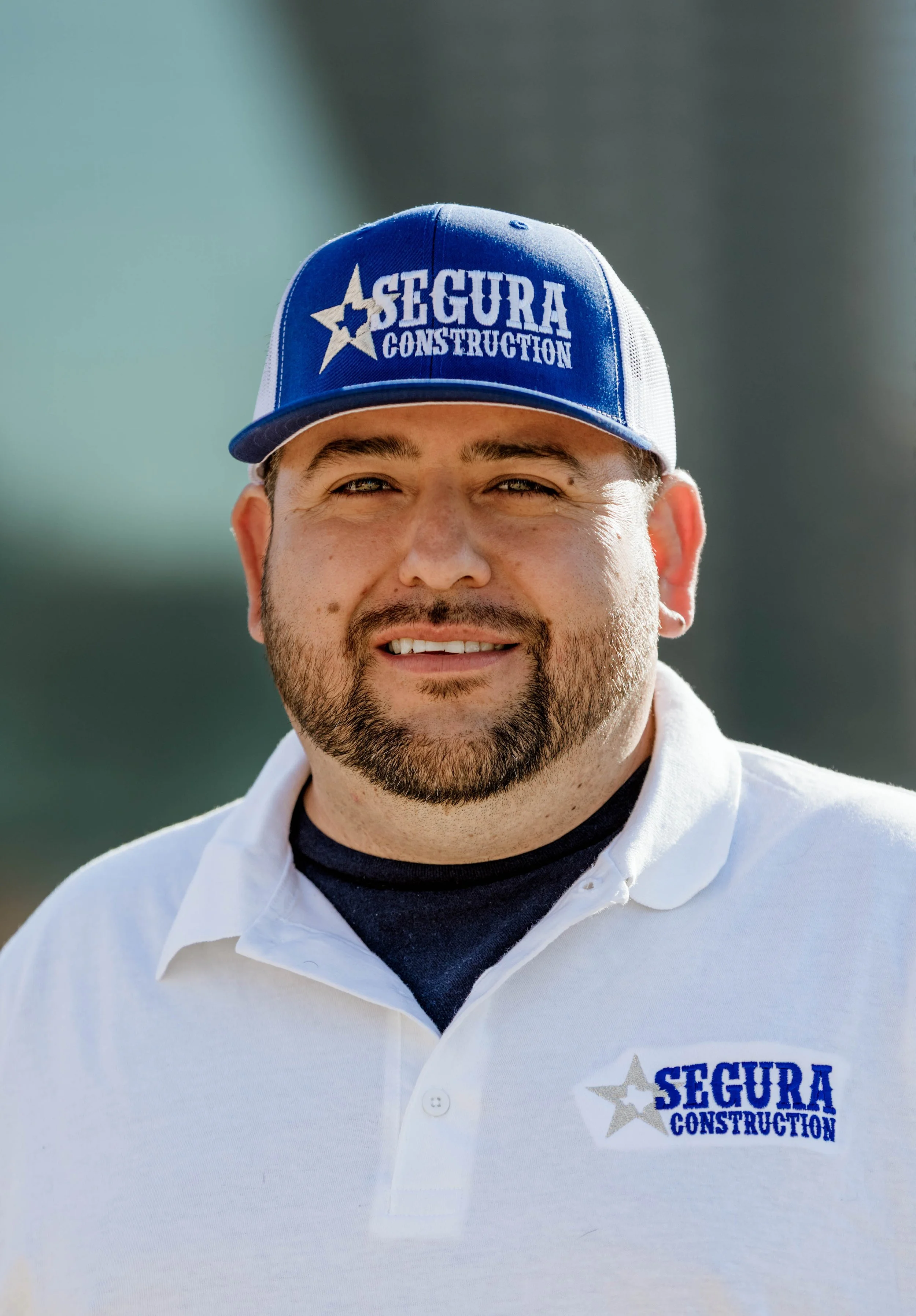 Man wearing a blue and white cap and white polo shirt with 'Segura Construction' logo.