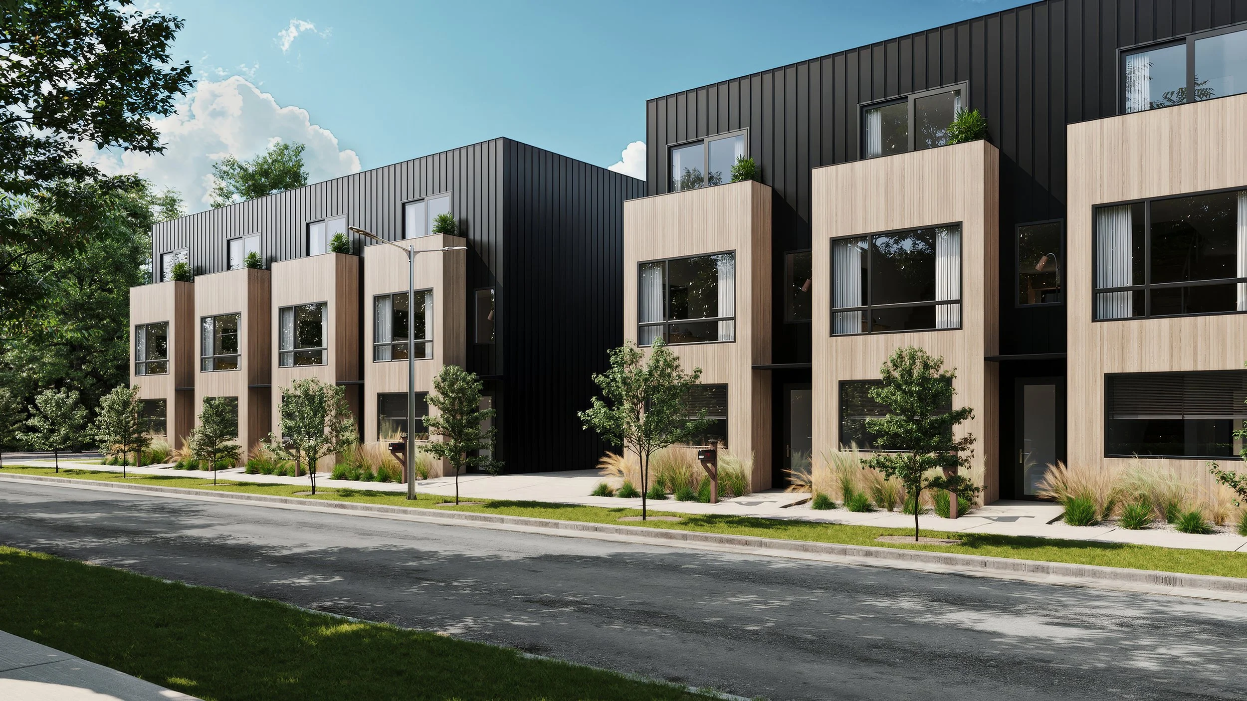 Modern townhouses, the Mo Town from MOMO by LuxMod, with black and wood exteriors, large windows, small front lawns with trees and grasses, sidewalk, street, and a blue sky with clouds.