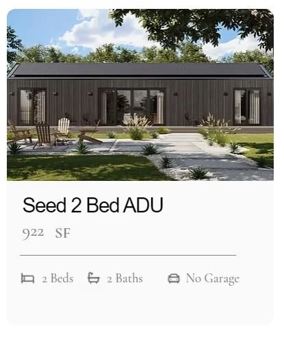 A modern, single-story ADU, the Seed from MOMO by LuxMod, with a dark exterior, large sliding glass doors, and a front porch with outdoor seating and landscaping, set against a backdrop of trees and blue sky.
