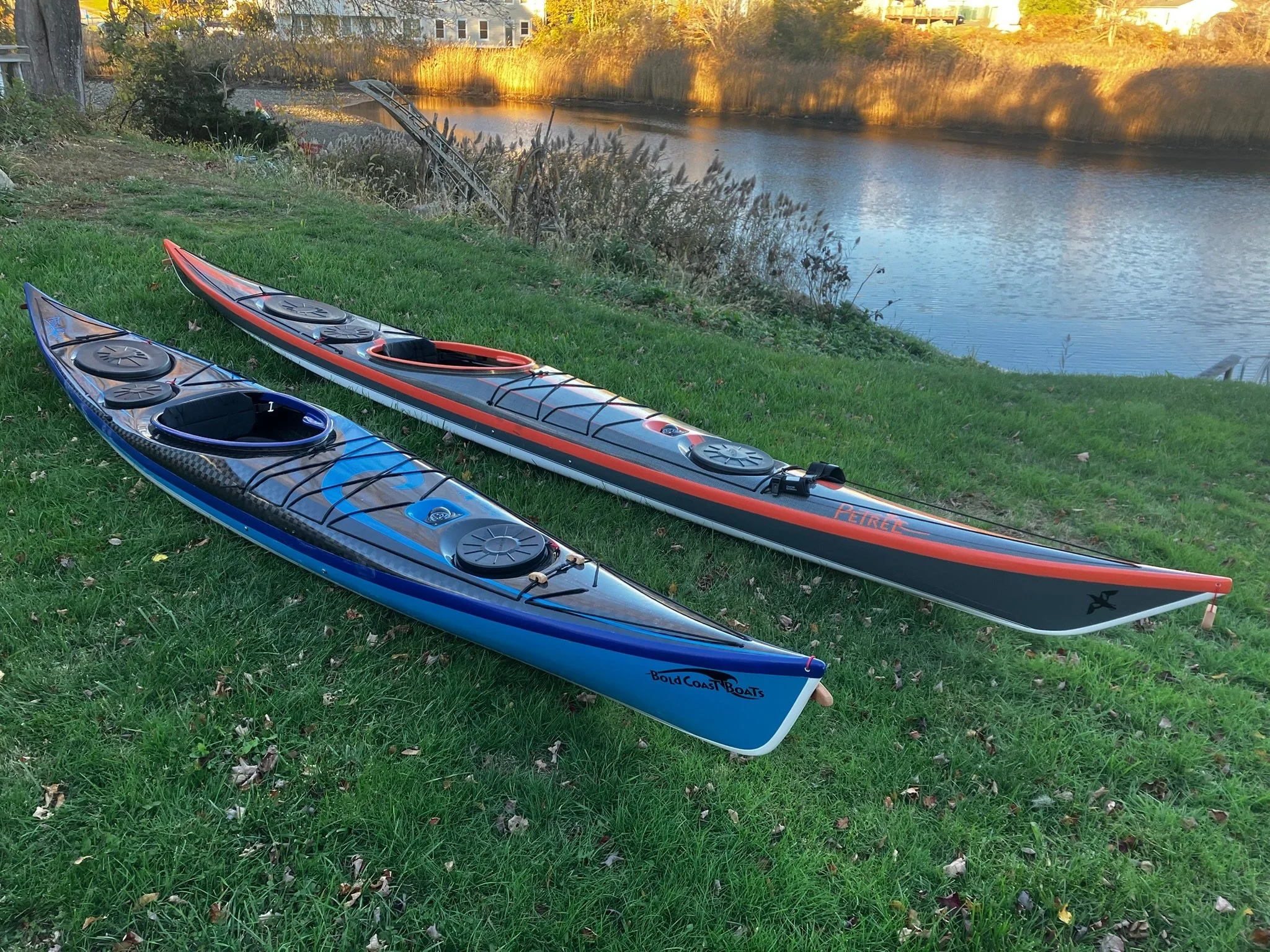 Two paddleboards, one blue and one gray with red accents, are resting on the grassy riverbank near the water.