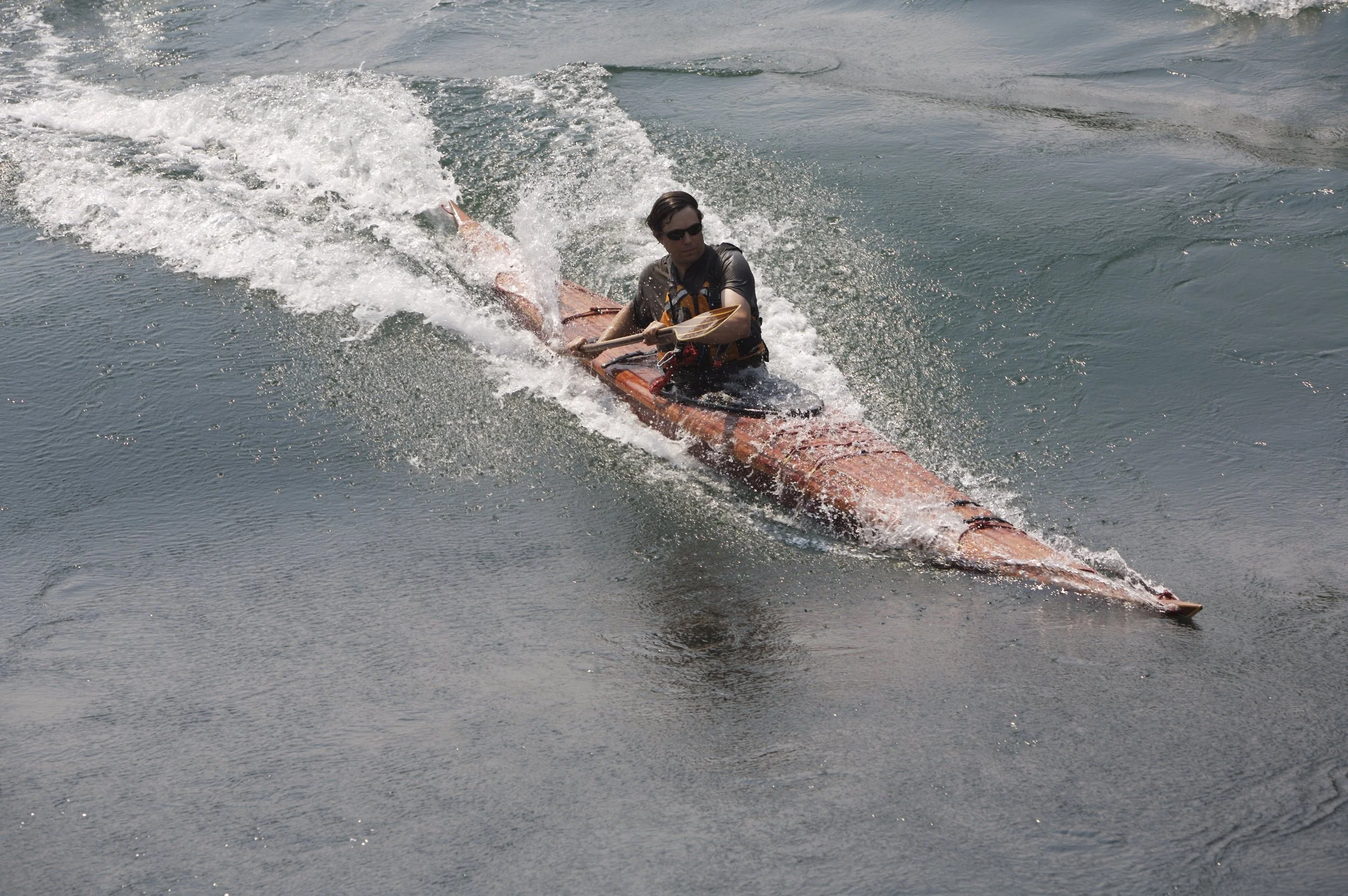 Person kayaking surfing a tidal falls, wearing a life jacket and sunglasses.