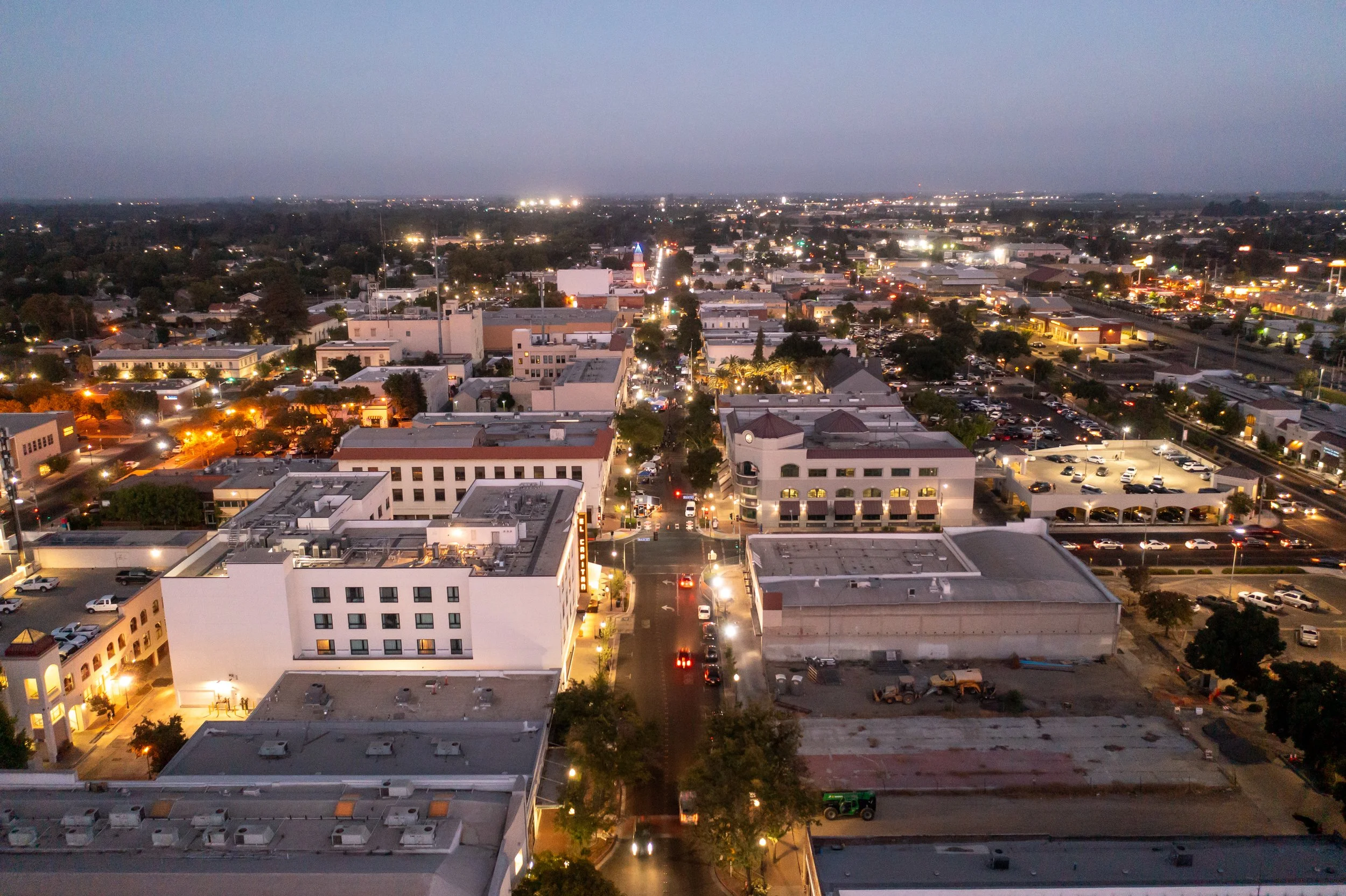An aerial night view of a city with illuminated buildings, streets, and cars, extending into the horizon under a dark sky.