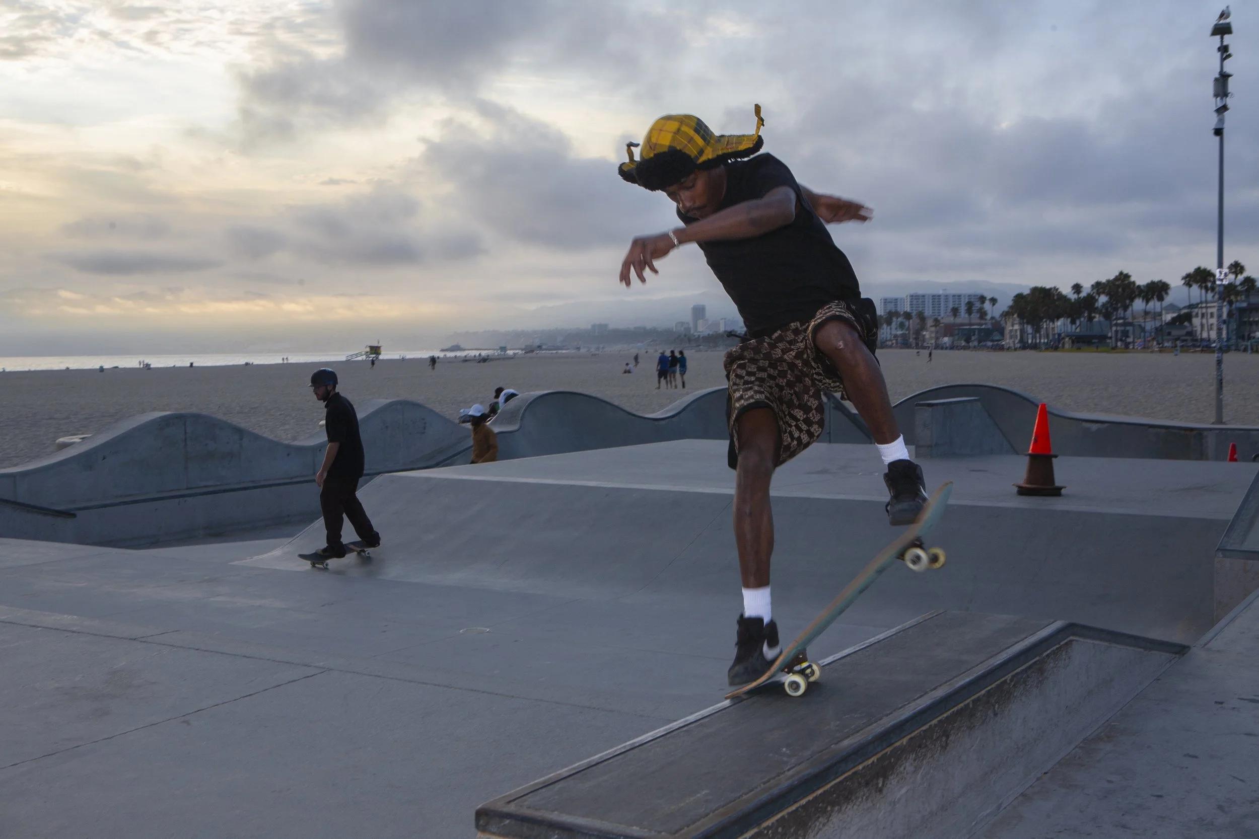 Skateboarder performing a trick at a skate park near the beach during sunset.