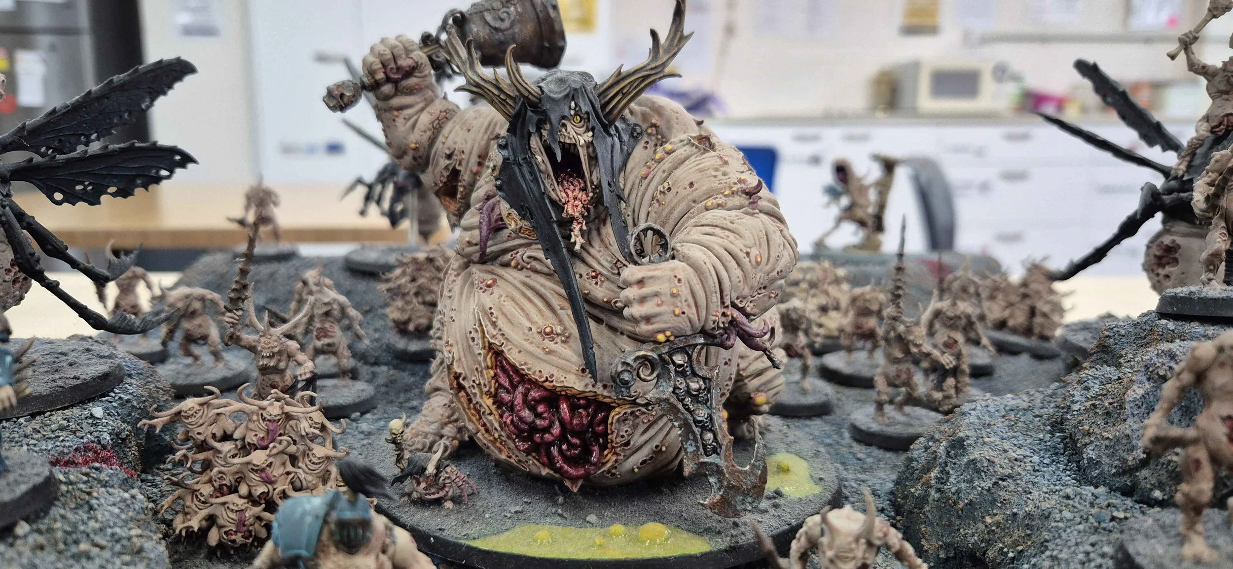 Detailed miniature painted figure of a monstrous creature with tentacles, sharp teeth, and multiple small figures around it, set on a textured base.