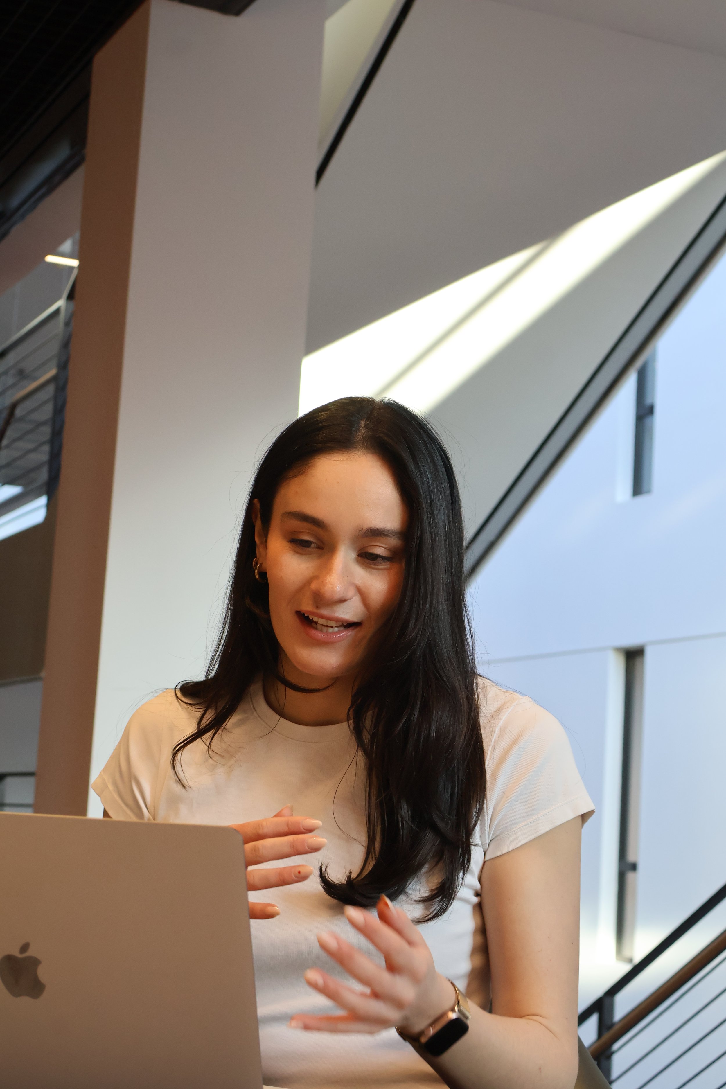 Junge Frau mit dunklen Haaren arbeitet an einem Laptop in einem modernen Gebäude.