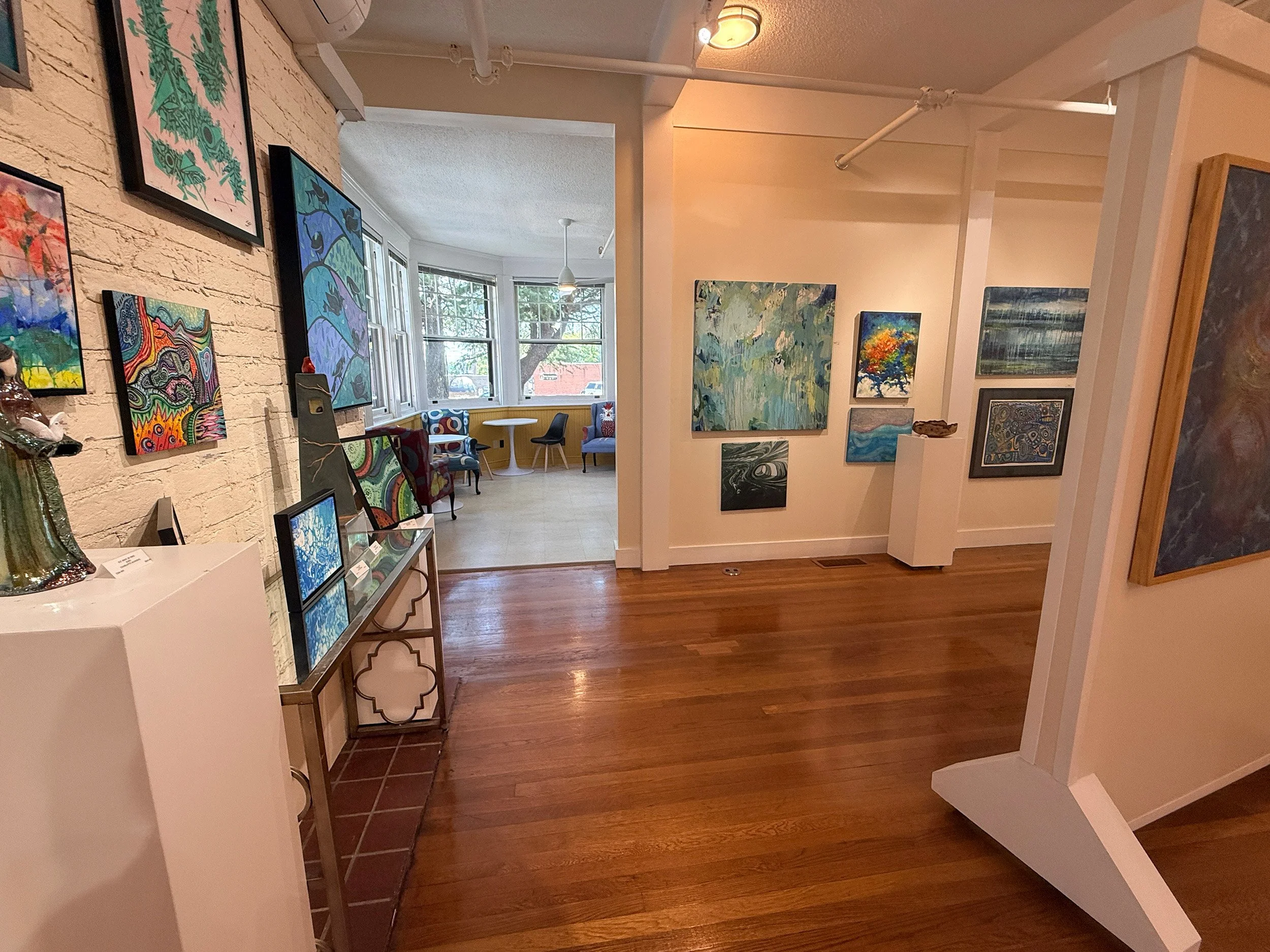 Marshall Muse Gallery with an array of multicolored abstract art images hanging on the walls and placed on tables and pedestals. Part of the August 2026 "Abstract Impressions" exhibit. Sip & See Cafe is also seen in the shot.