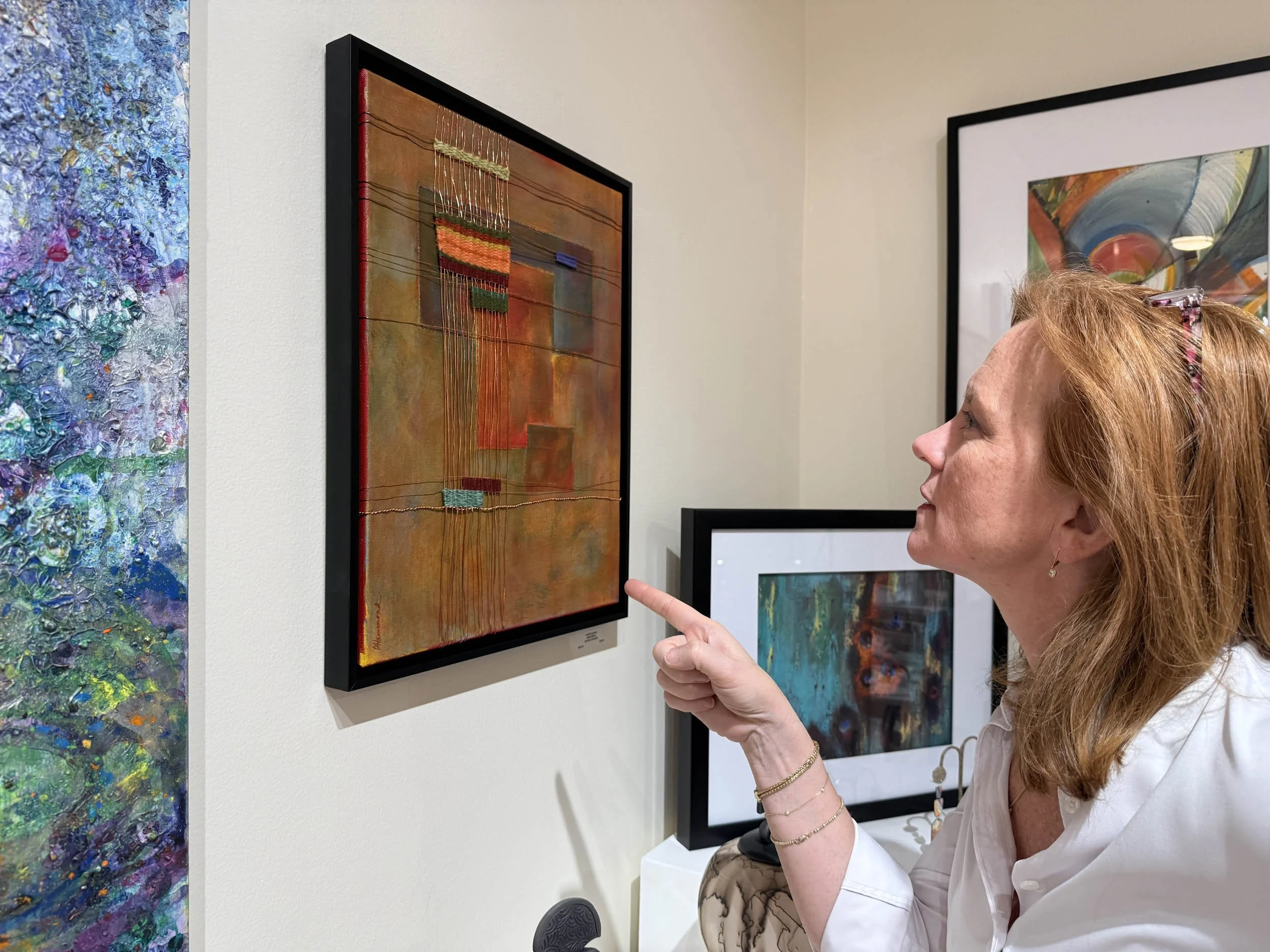 Tracey Marshall, TMMG owner, points to abstract submission by Belinda Hammond. It is part of the "Abstract Impressions" exhibit. Notice that other artwork in the shot is also appropriate to the abstract artwork theme for our August 2026 show.