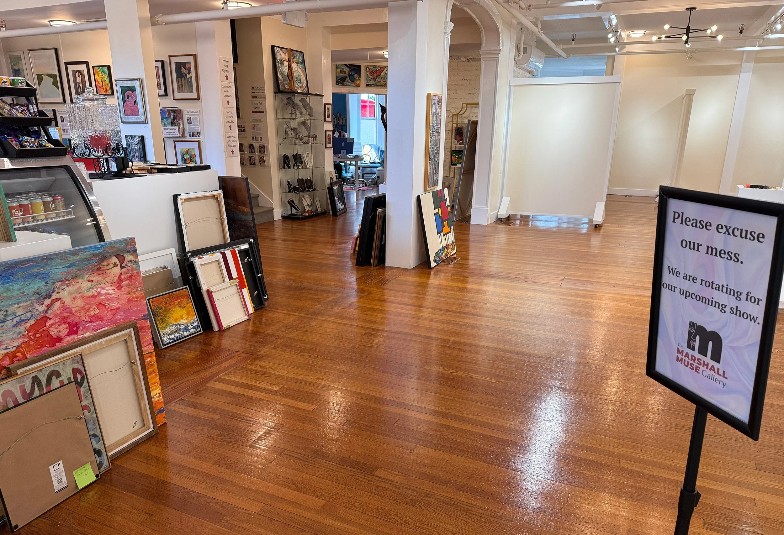 "Please Excuse Our Mess" sign at the end of July 2026 when The Marshall Muse Gallery's August exhibit, "Abstract Impressions" is being hung. Walls are blank and art is stacked carefully on the floors awaiting its place in the show.
