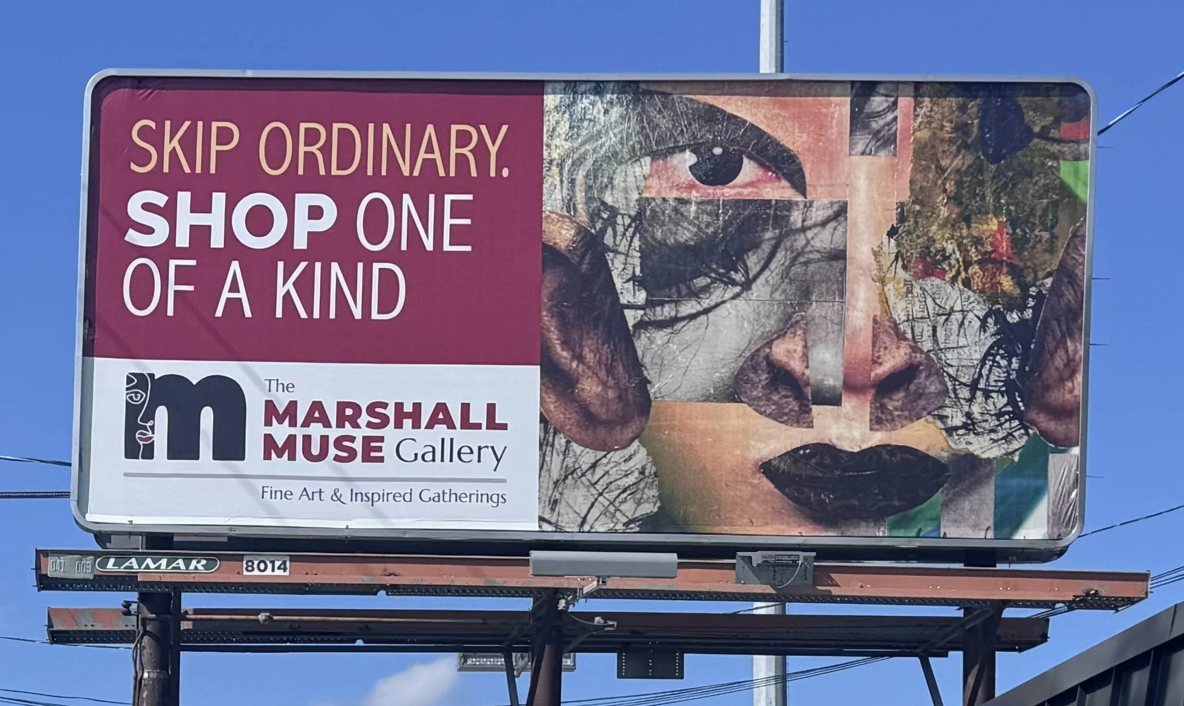 Our billboard on Battleground avenue. The left side features our logo and "Skip Ordinary. Shop One of a Kind". On the right is a bold, collaged face. Blue sky in the background.