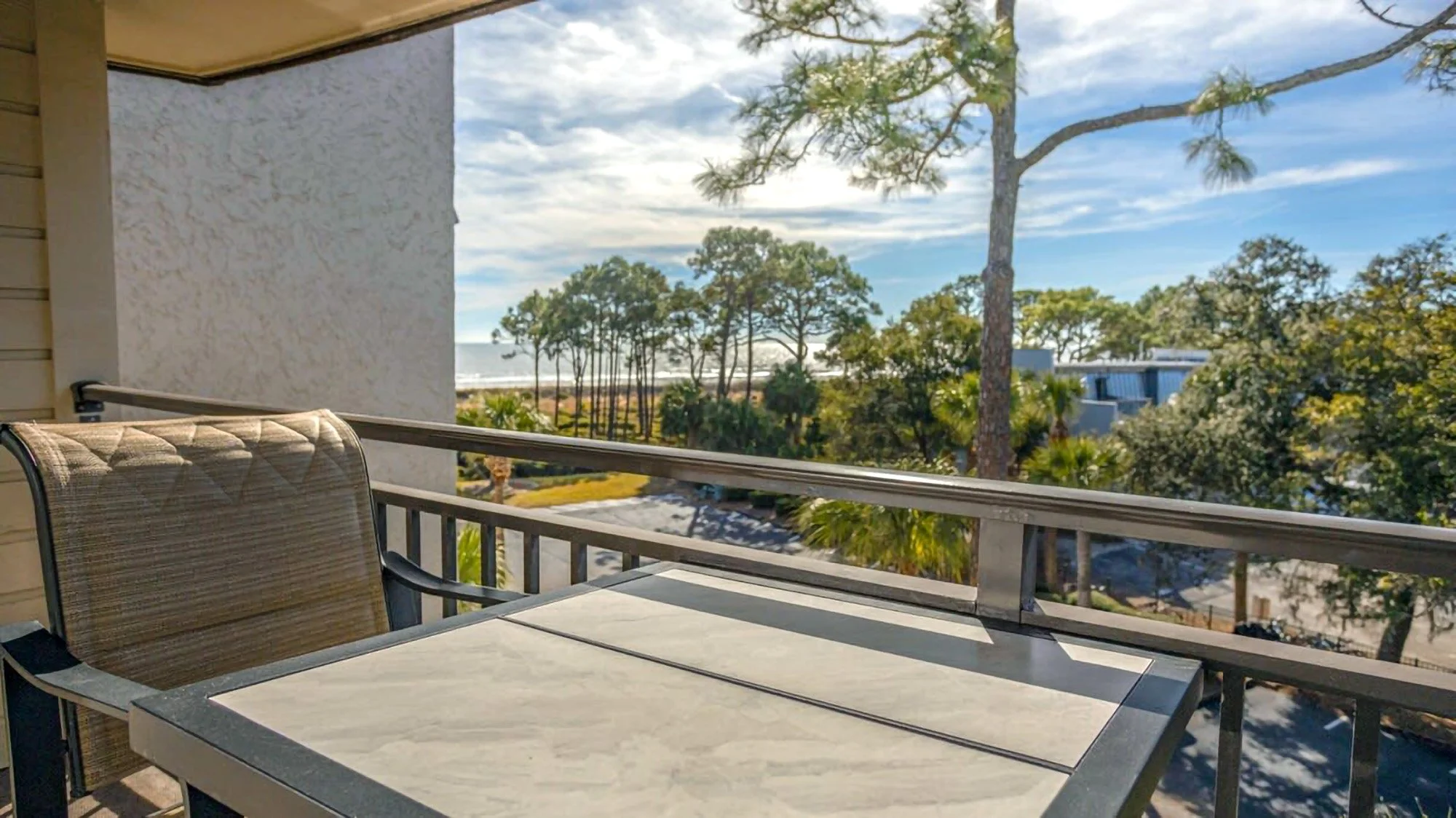Balcony with chair and table overlooking trees and sea view.
