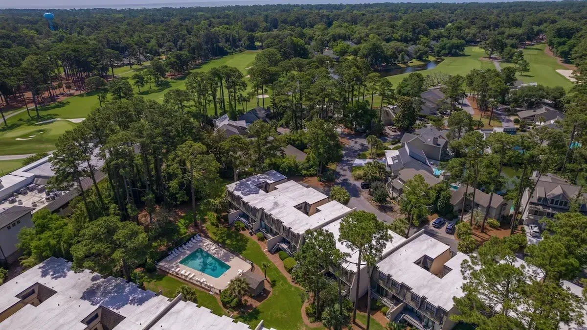 Aerial view of residential neighborhood with a golf course and outdoor swimming pool surrounded by trees.