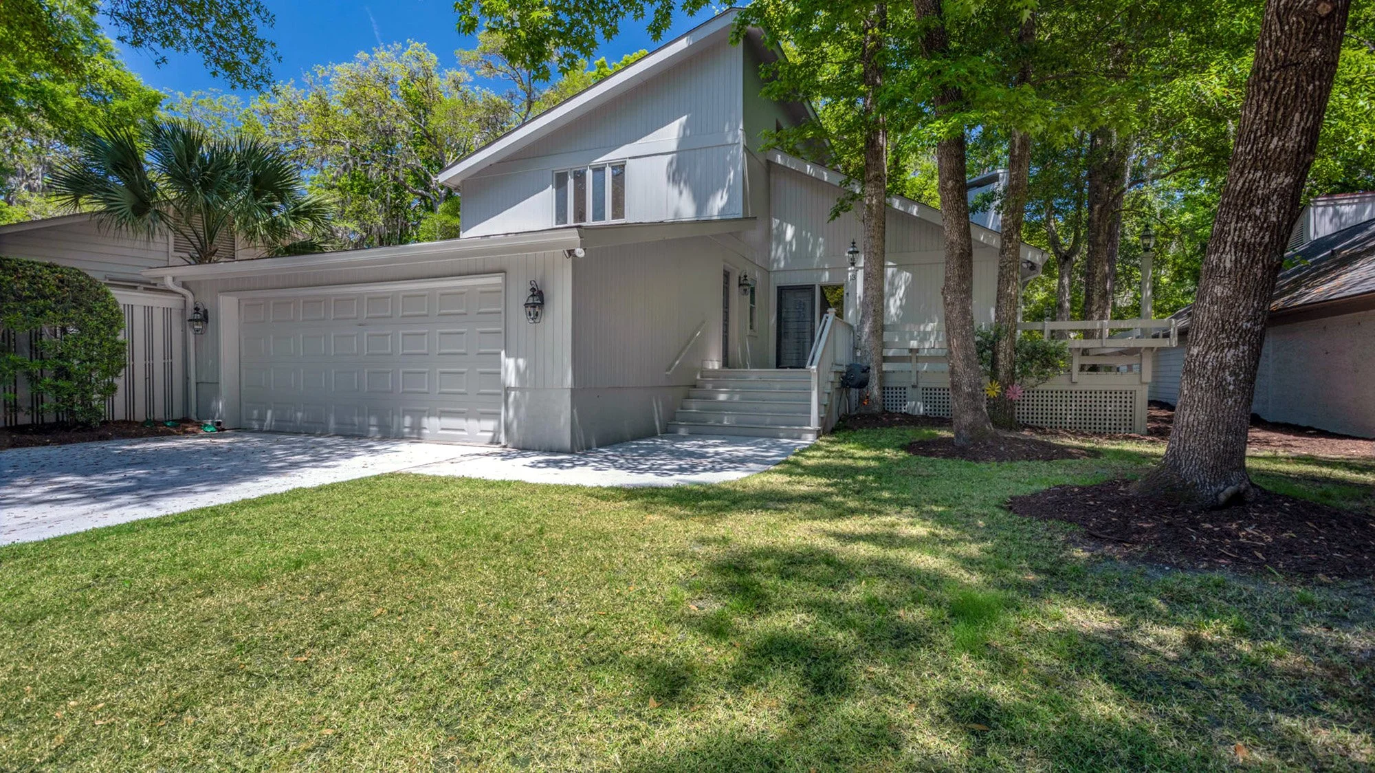 Modern house with garage and front yard, surrounded by trees on a sunny day.