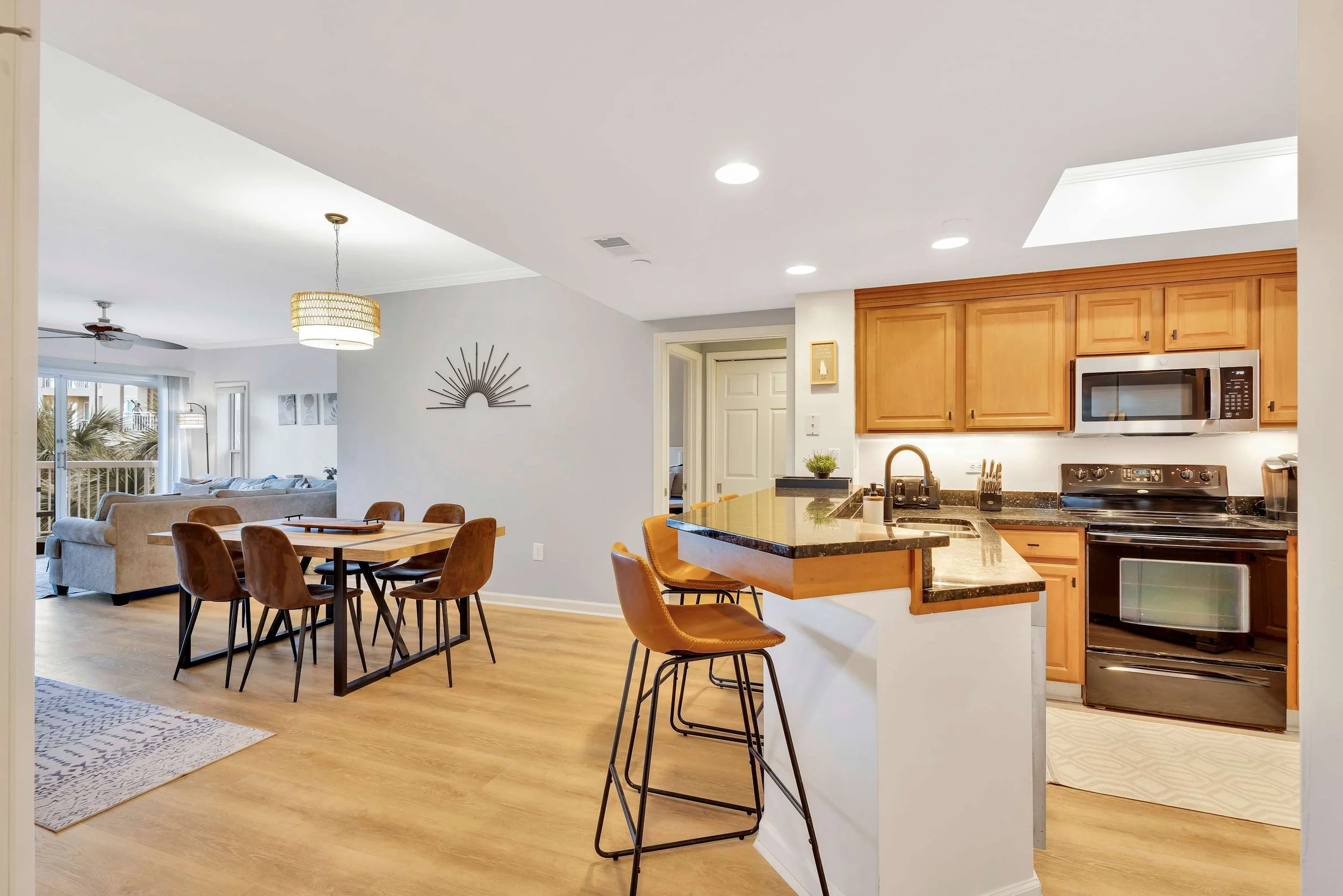 Modern open-concept kitchen and dining area with wooden cabinets, stainless steel appliances, a dining table with six chairs, and a breakfast bar with stools.