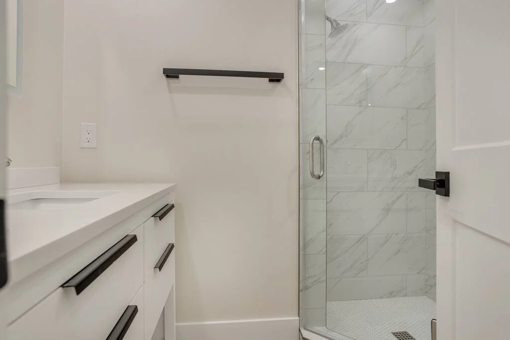 Modern bathroom with marble-tiled shower, glass door, white vanity with black hardware, and towel bar.