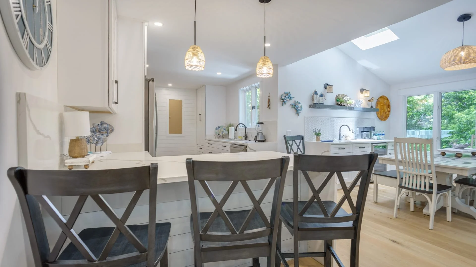 Modern kitchen interior with island, bar stools, pendant lights, skylight, and dining area with white and gray decor.